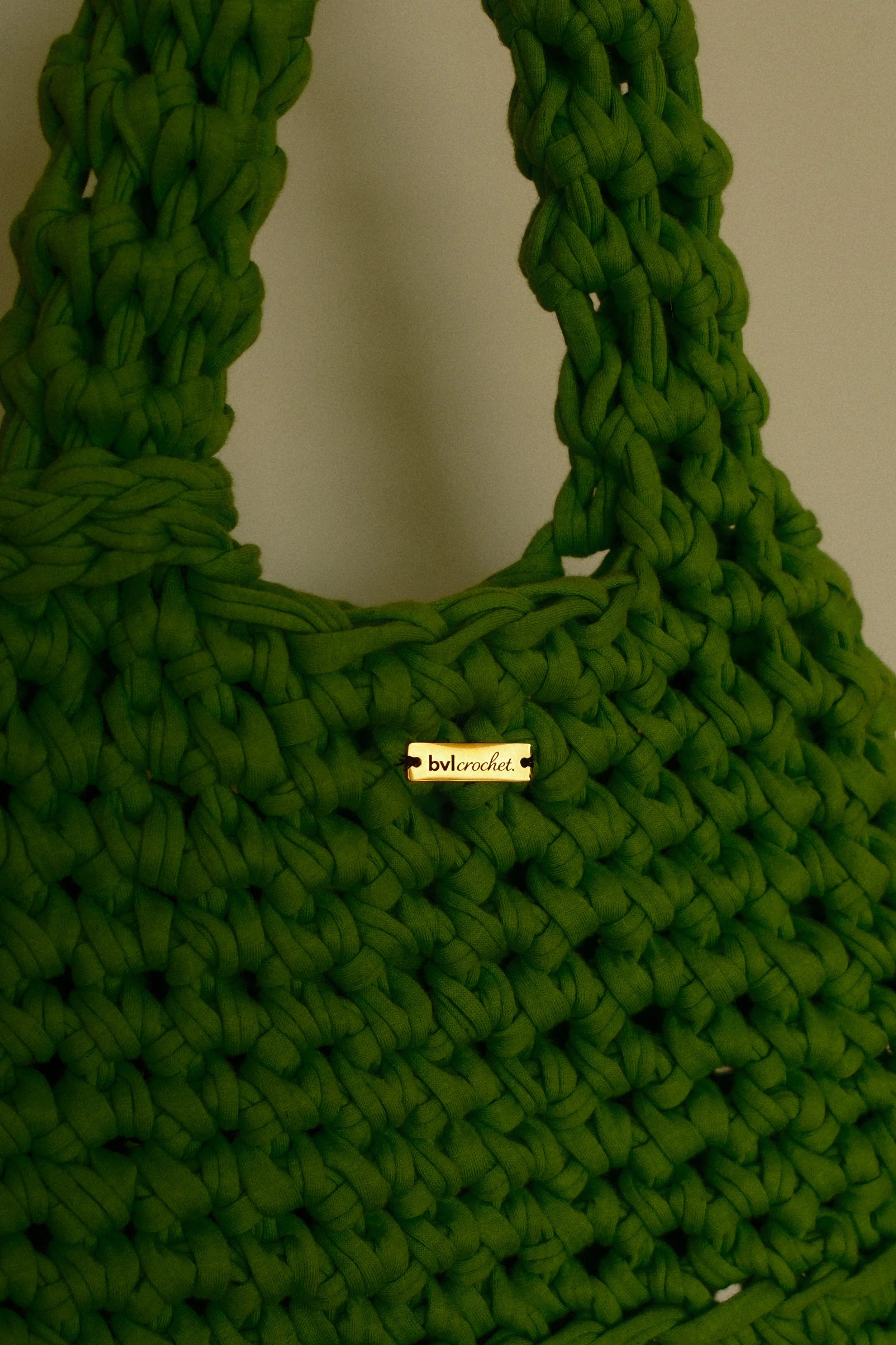 Close-up of a green crocheted handbag with a label that reads 'bvl crochet' attached to it.