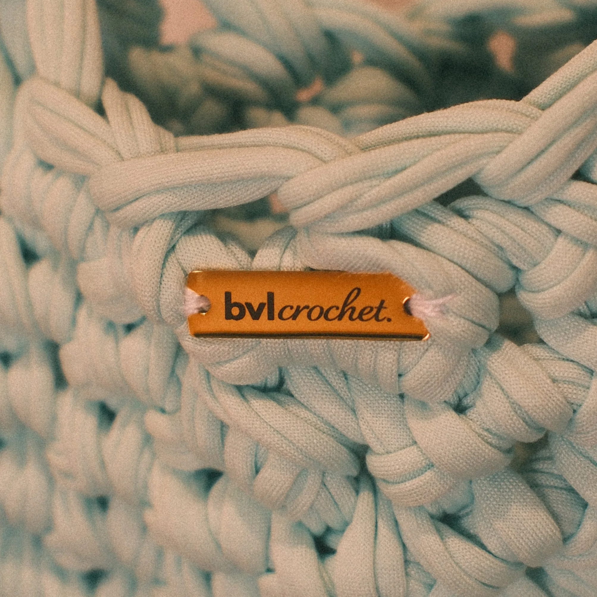 Close-up of embroidered fabric with a tag that reads 'by crochet' in orange.
