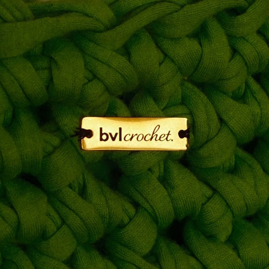 Close-up of a green knitted item with a small label that reads 'bvlcrochet'.