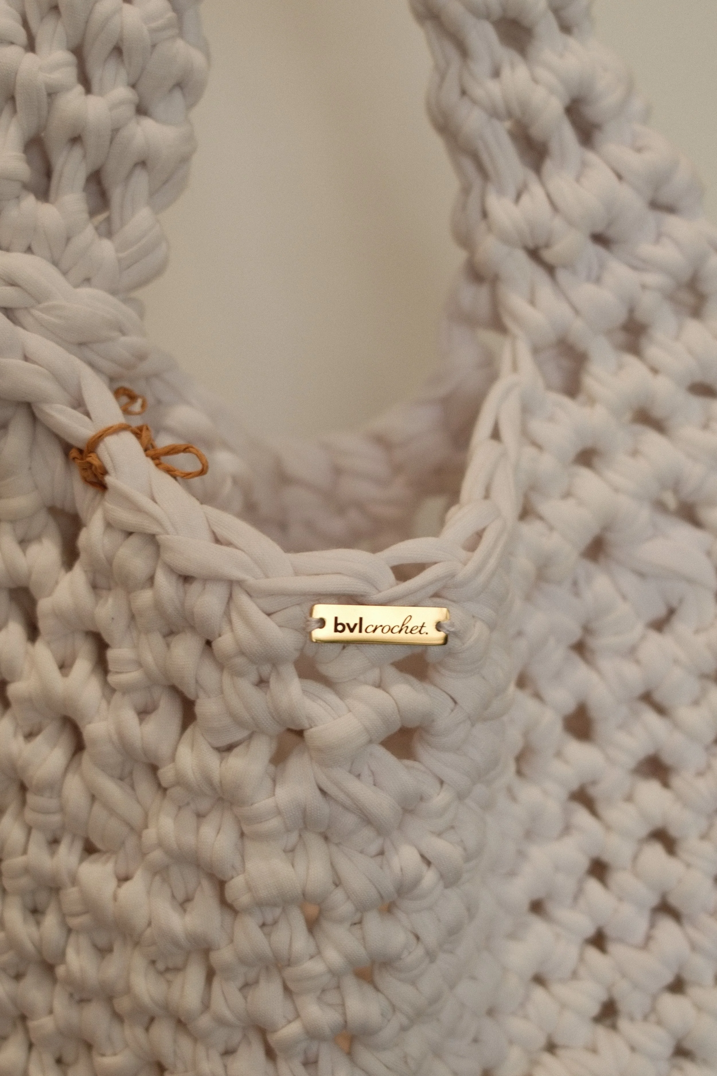 Close-up of white woven crocheted fabric with a small gold tag that reads "bvl crochet" attached to it.