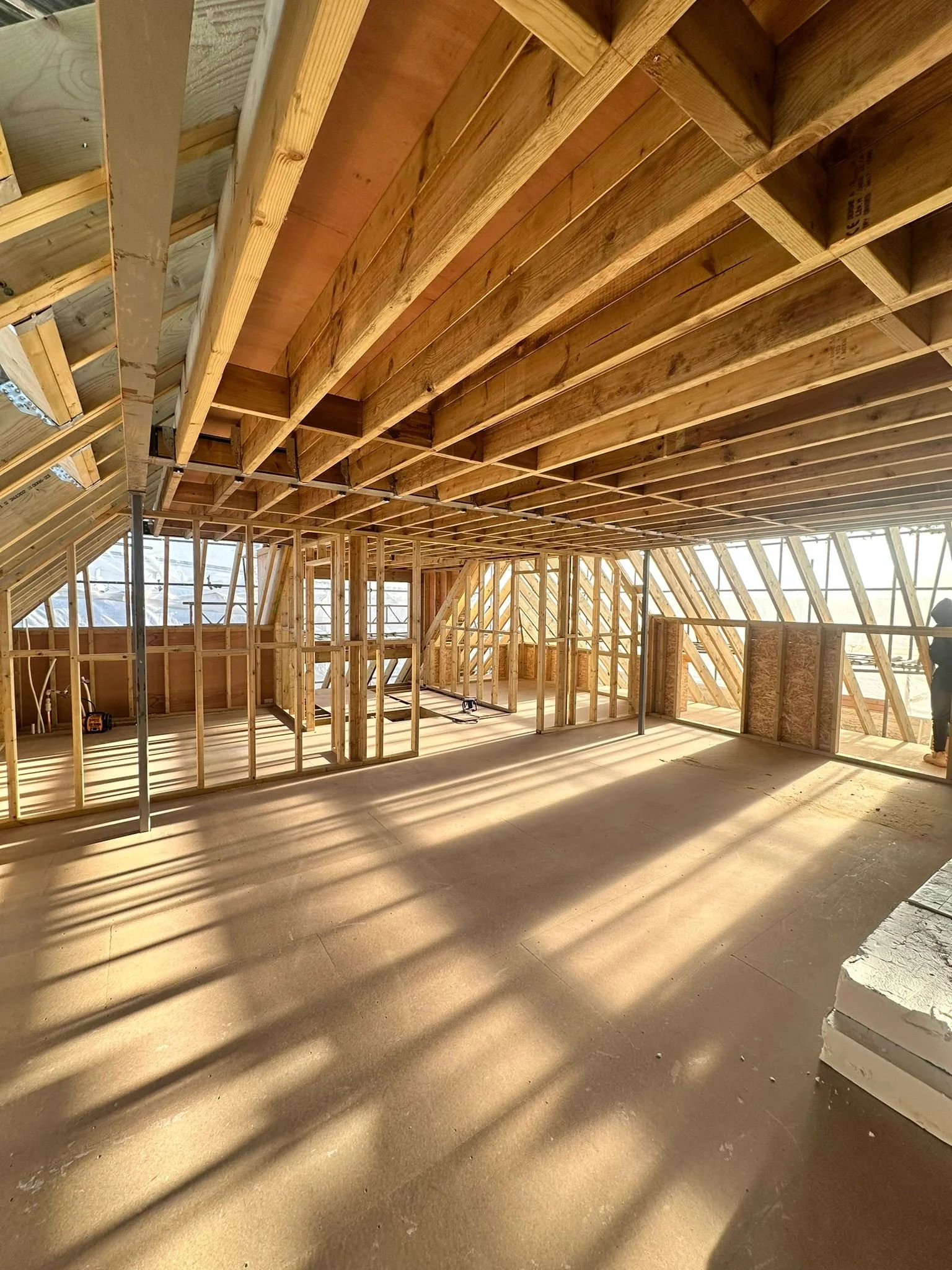 Wood framing of a building under construction with sunlight casting shadows on the floor.