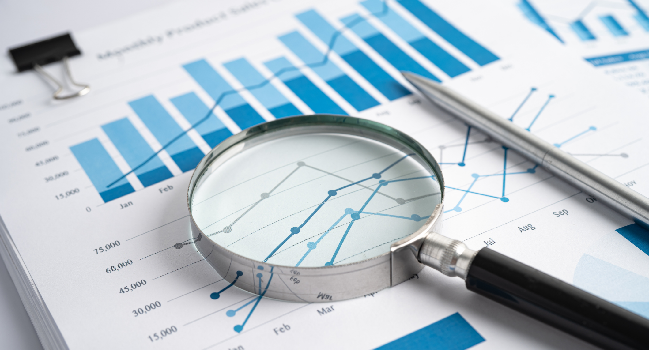 Business charts with bar graphs and line graphs on paper, magnifying glass and pen, white background.