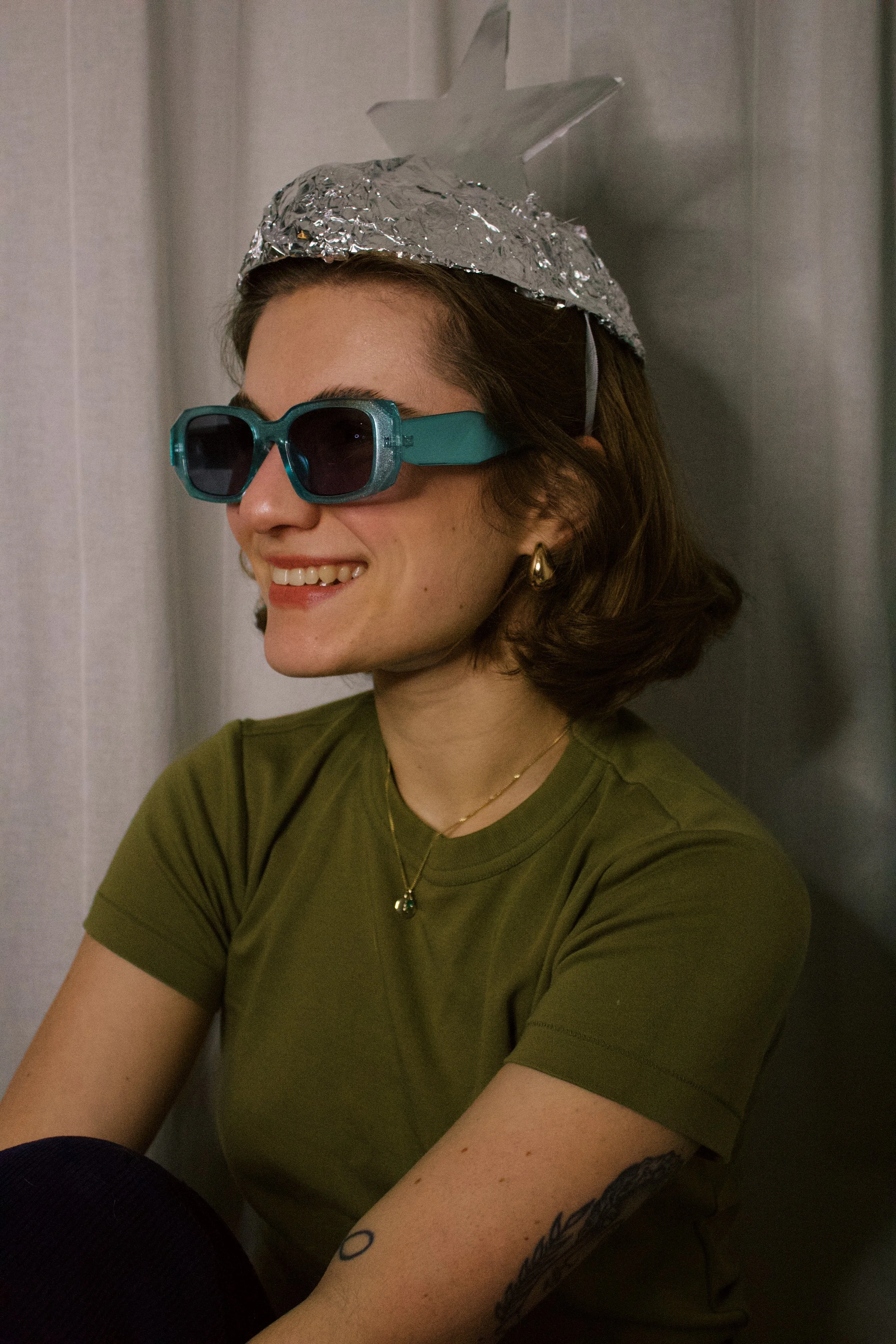 A woman smiling while wearing blue sunglasses and a silver paper hat shaped like a spaceship.