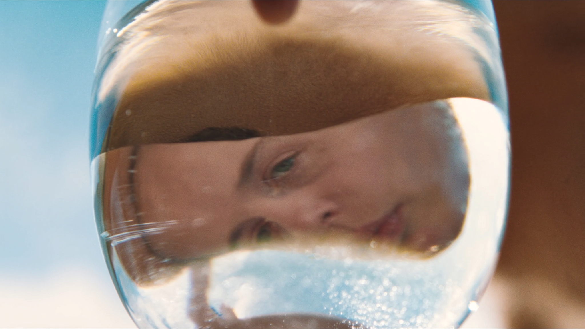 Close-up of a woman's face reflected in the surface of a clear glass of water