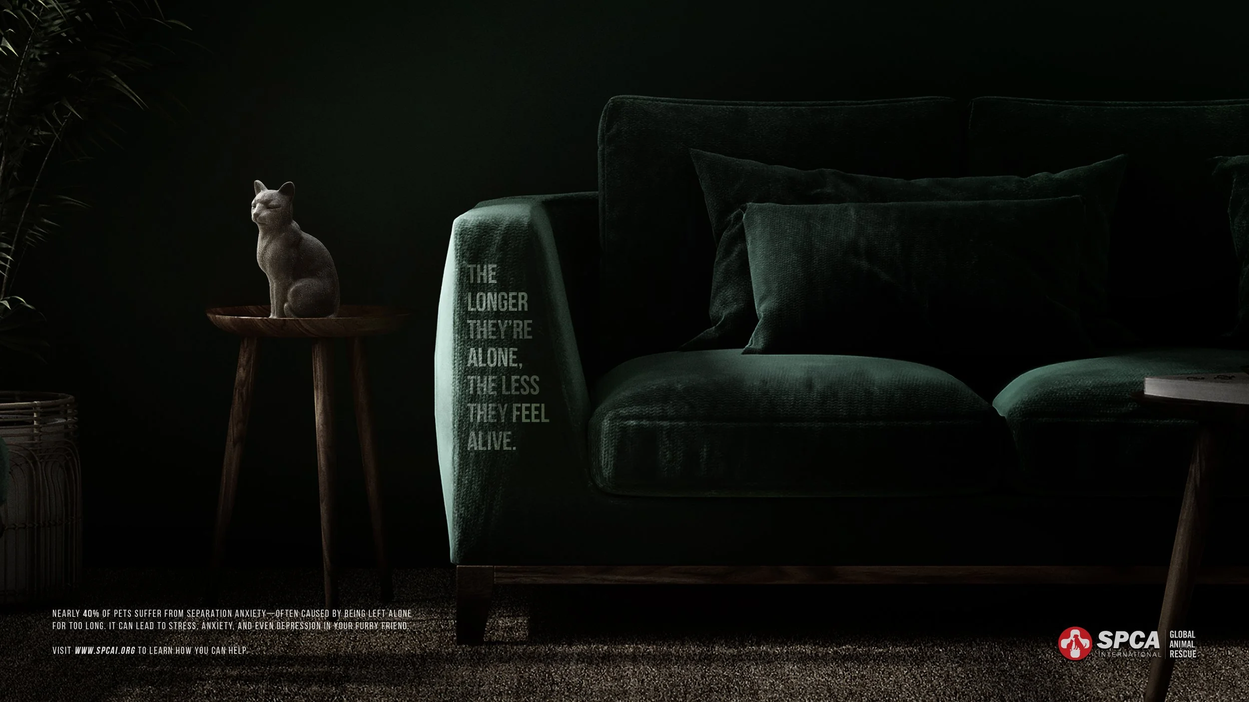 A dark green velvet sofa with matching pillows, a beige blanket with text, and a small wooden cat figurine on a side table, with a small amount of greenery and a logo in the bottom right corner.