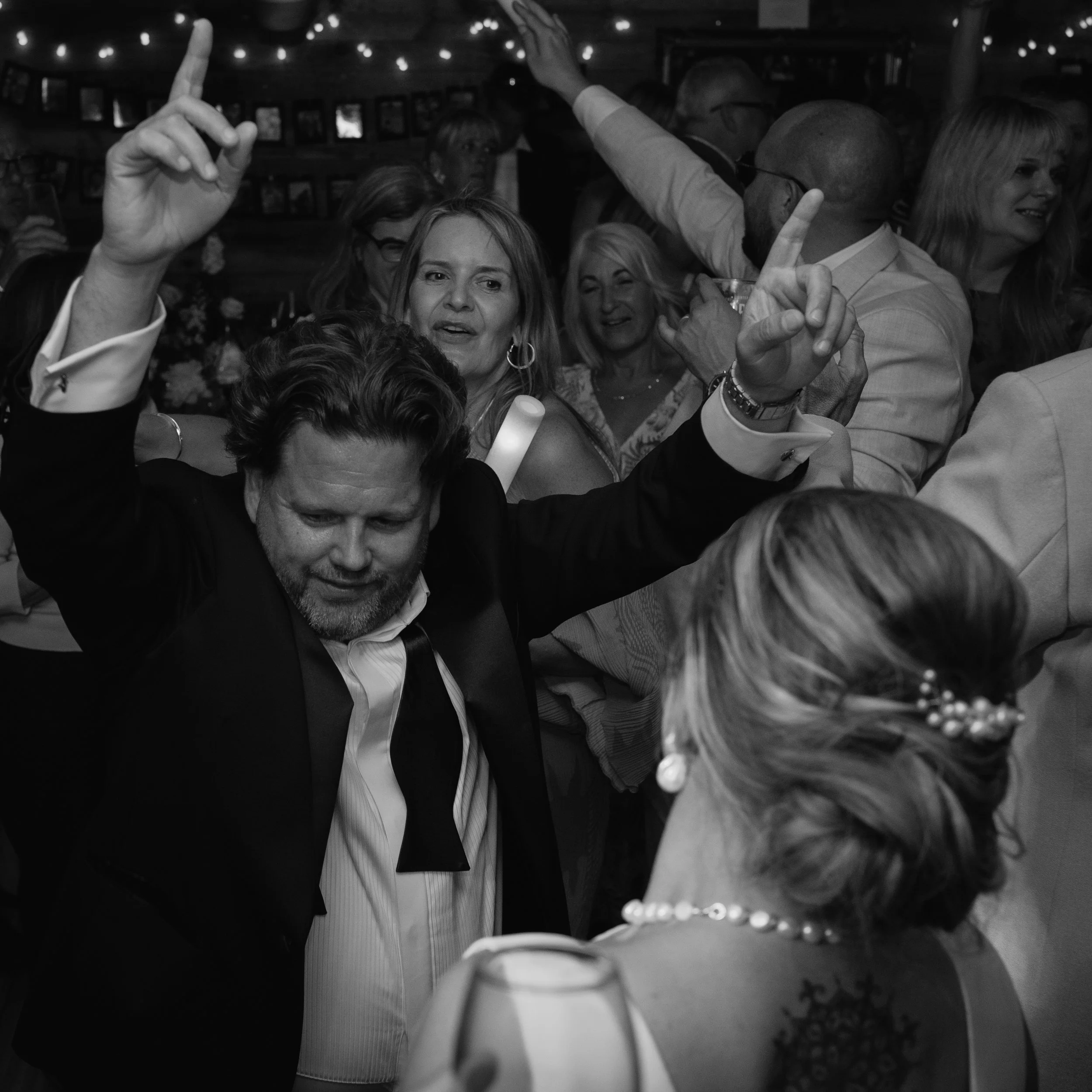 People dancing at a celebration with string lights and wedding decorations in the background.