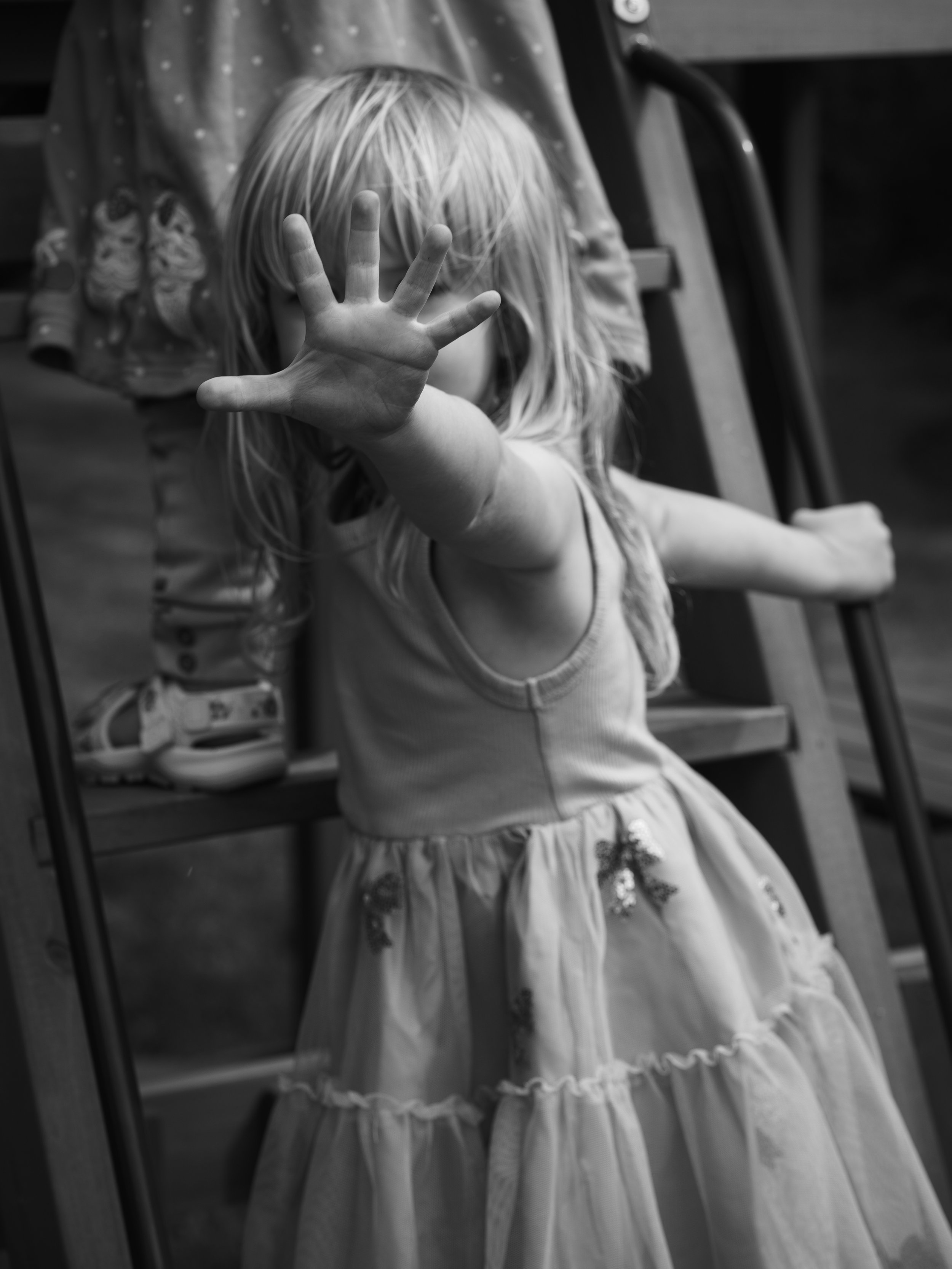 A young girl with long hair reaching out to the mirror, wearing a dress with floral embroidery.