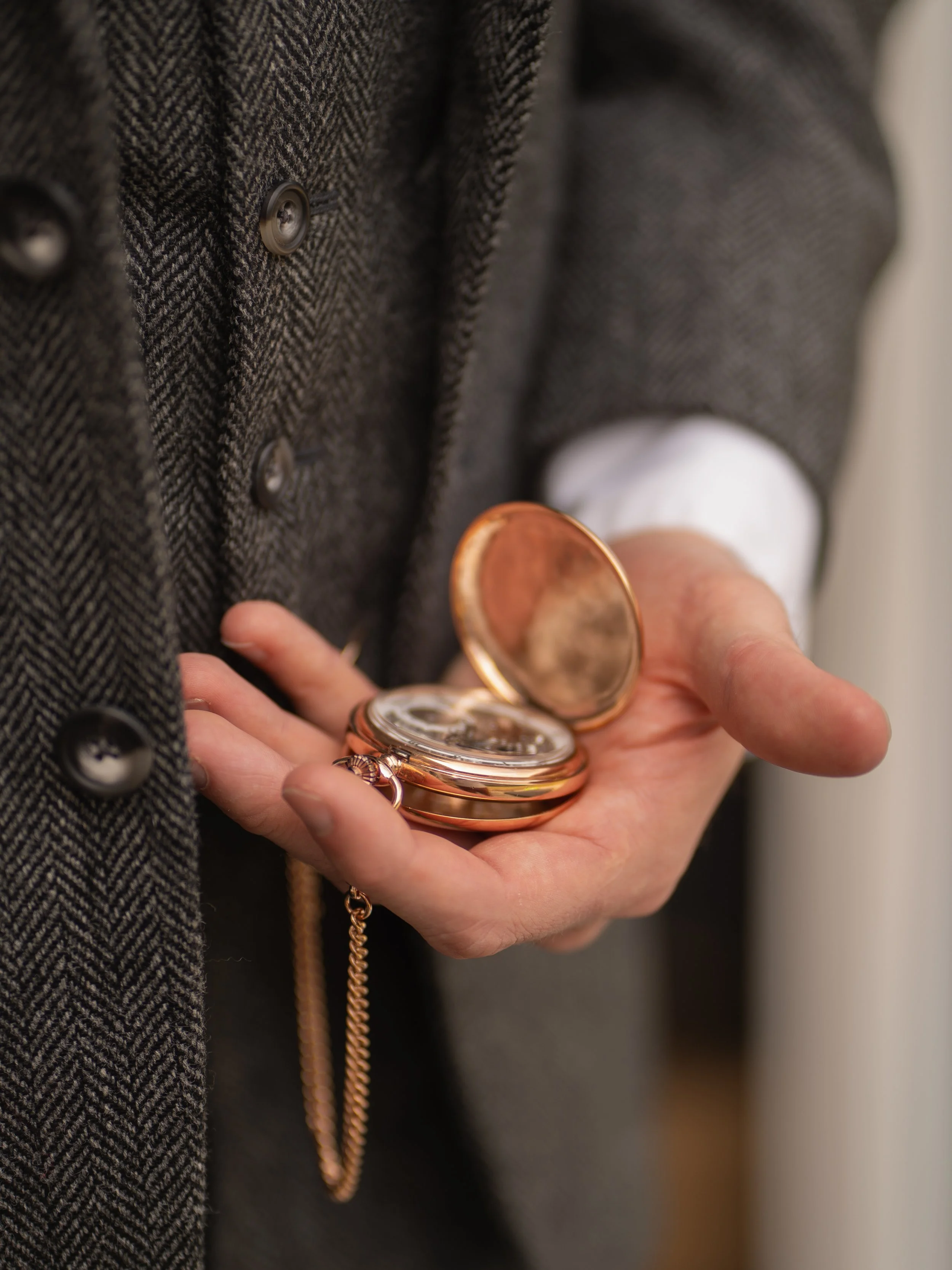 Close-up of a person holding vintage pocket watches with a gray tweed coat in the background.