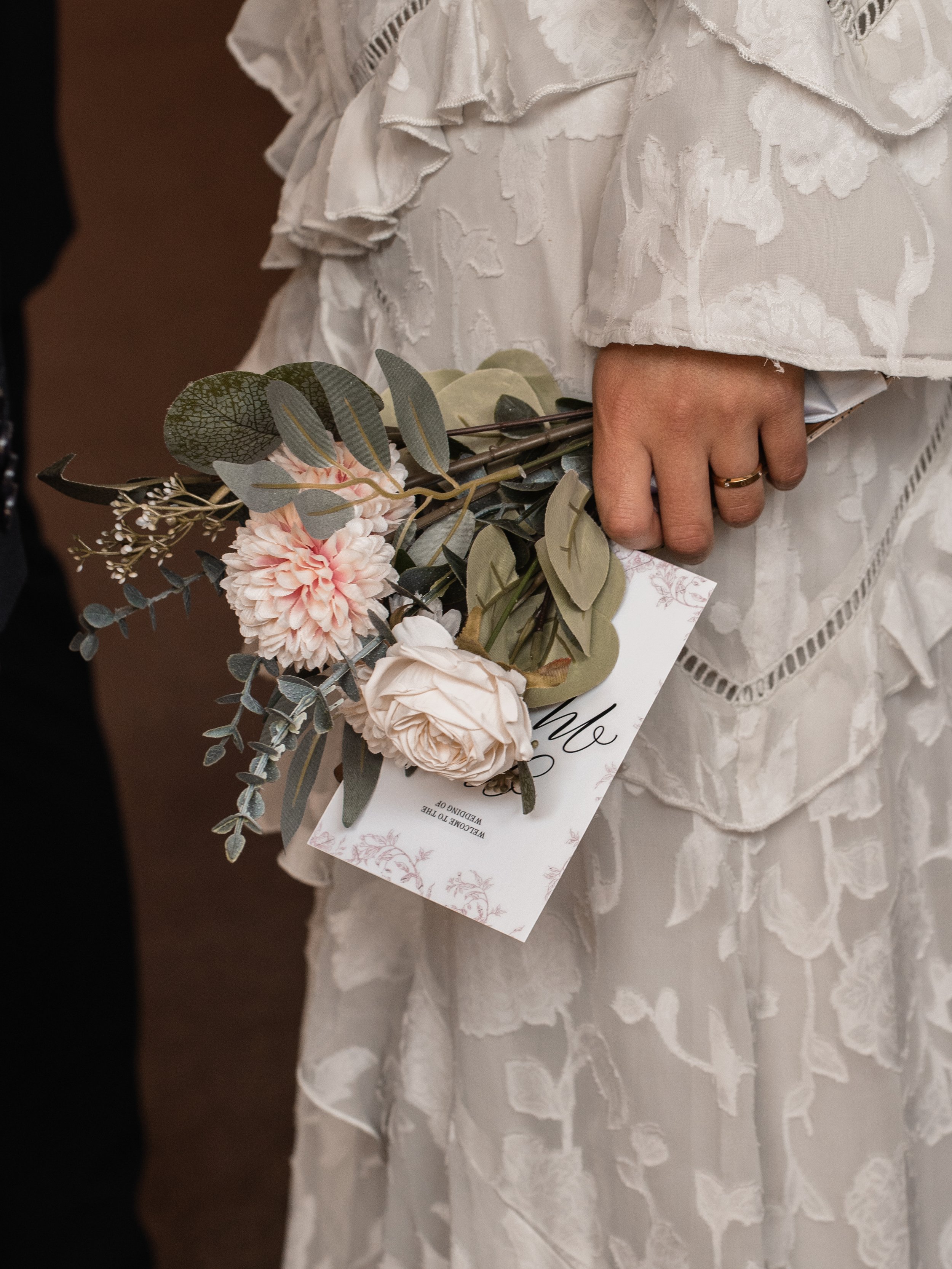 Person wearing a white lace dress holding a small bouquet of flowers, including pink and white roses and greenery.