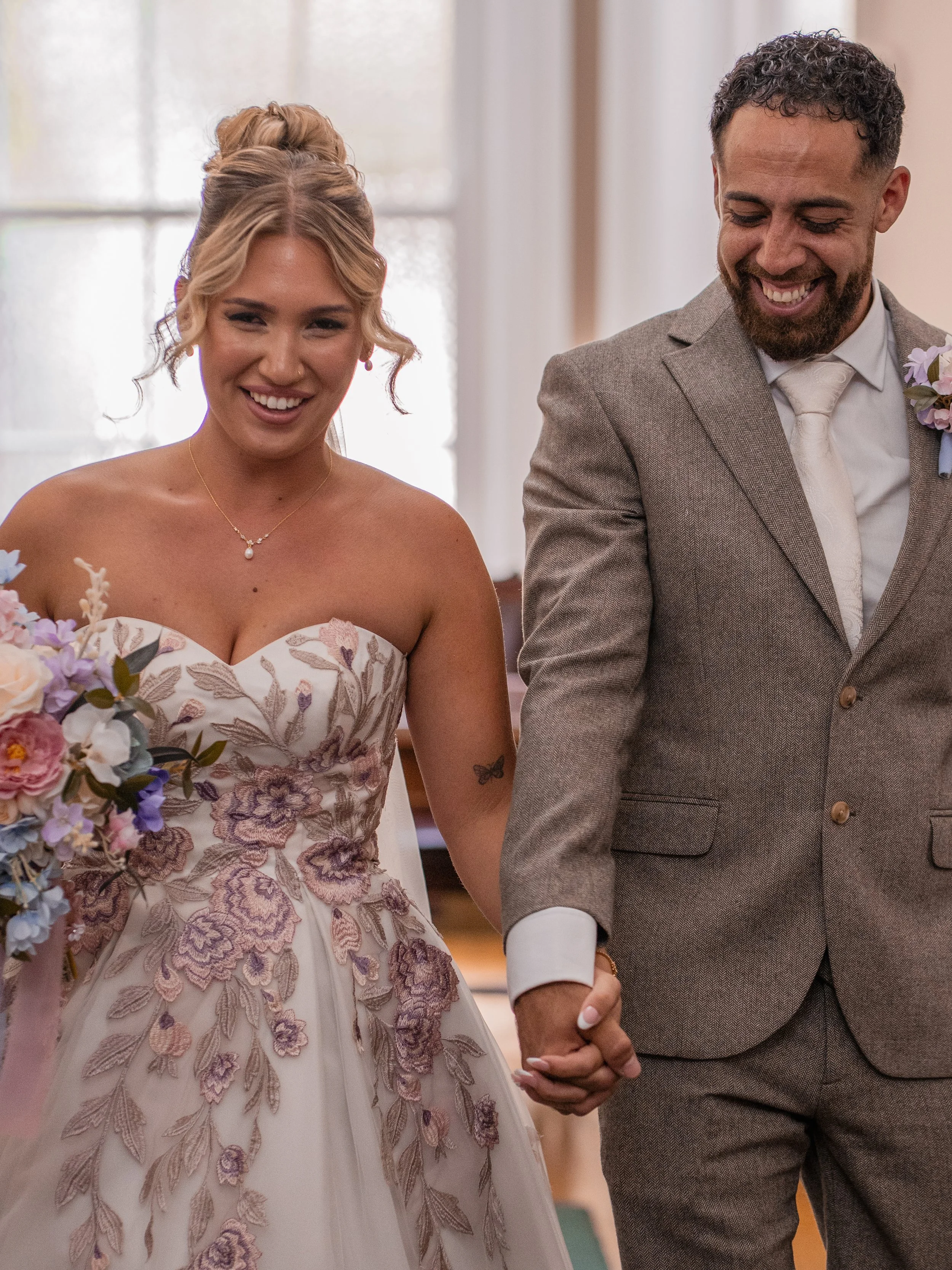 A smiling bride and groom holding hands during their wedding ceremony, walking down the aisle in a church or wedding venue.