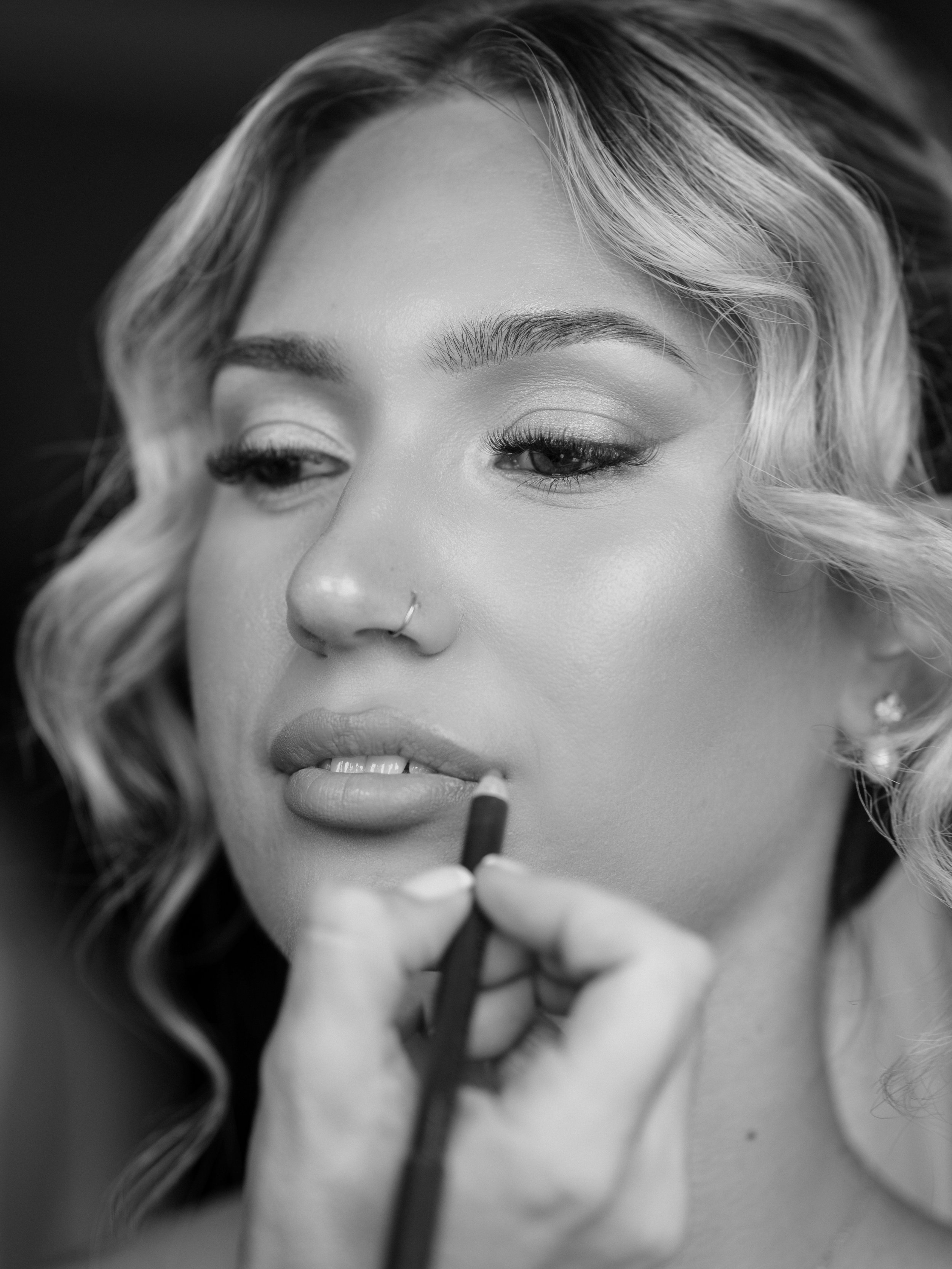 A woman applying lipstick, close-up of her face in black and white.