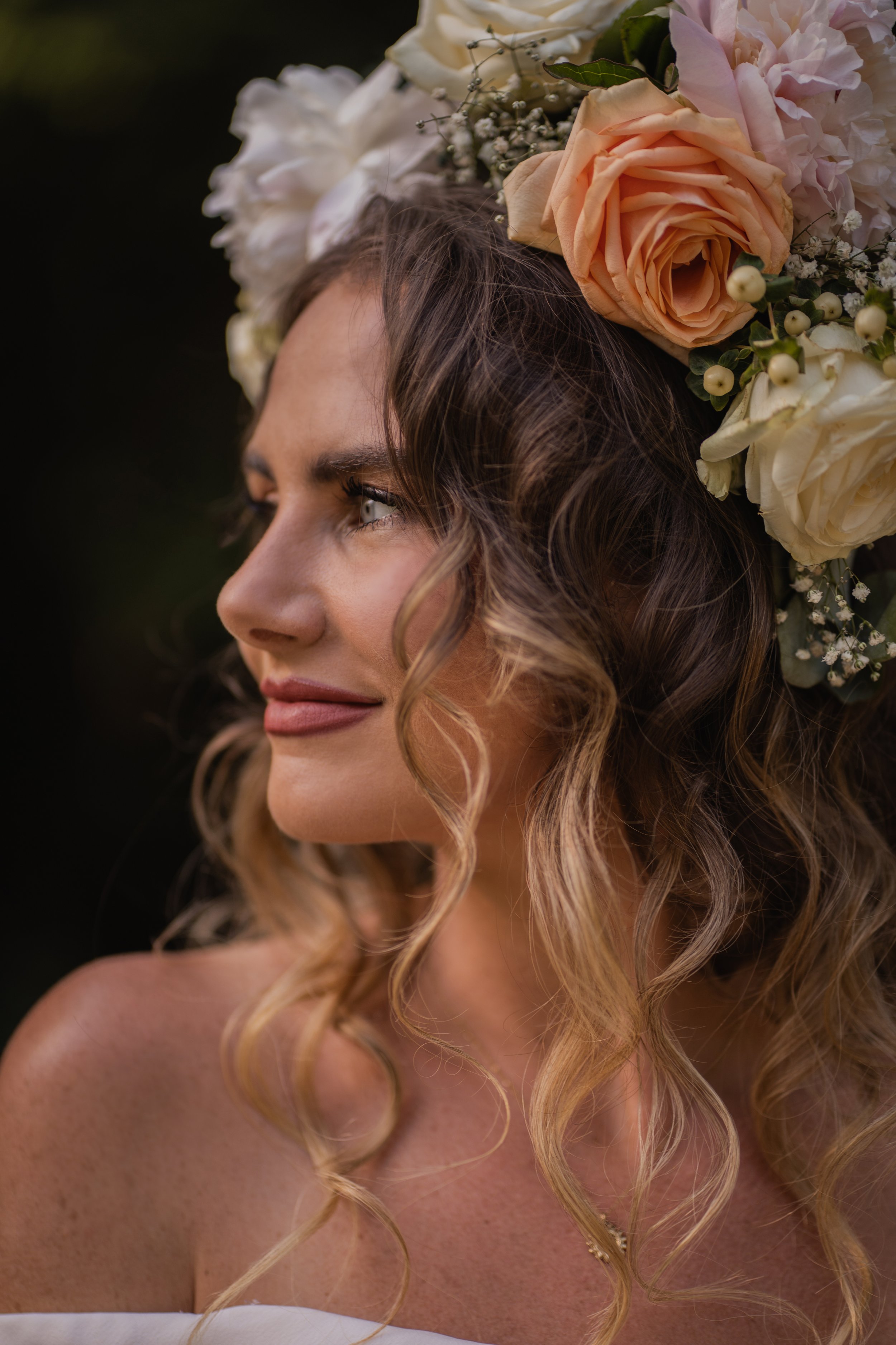 A woman with curly, blonde hair wearing a floral crown made of peach roses, white flowers, and small berries.