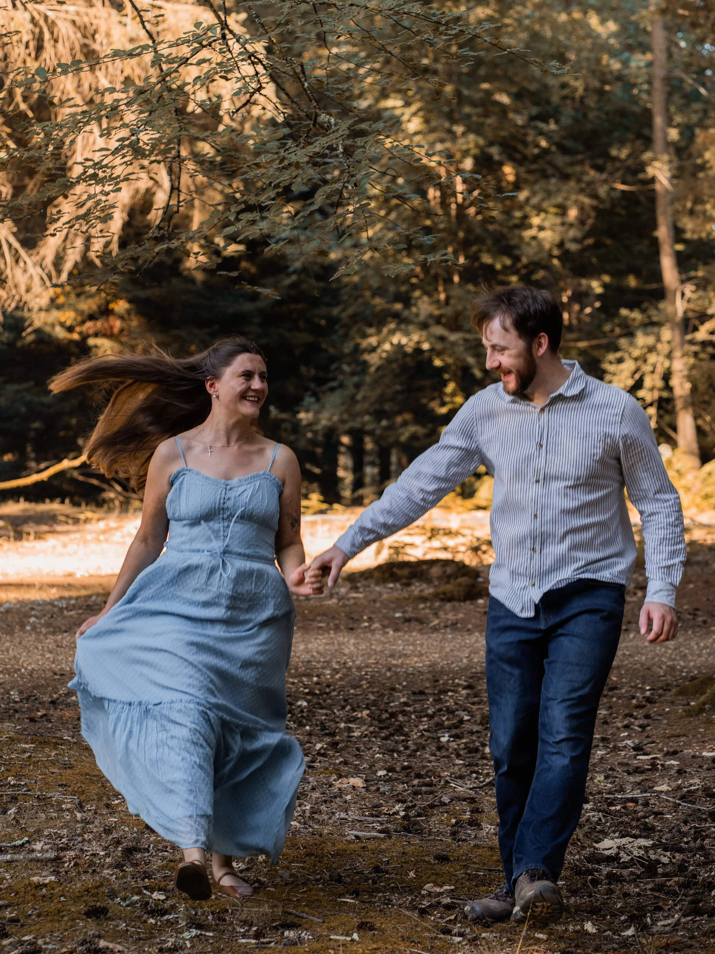 A couple holding hands and walking through a forest during autumn, smiling and enjoying each other's company.