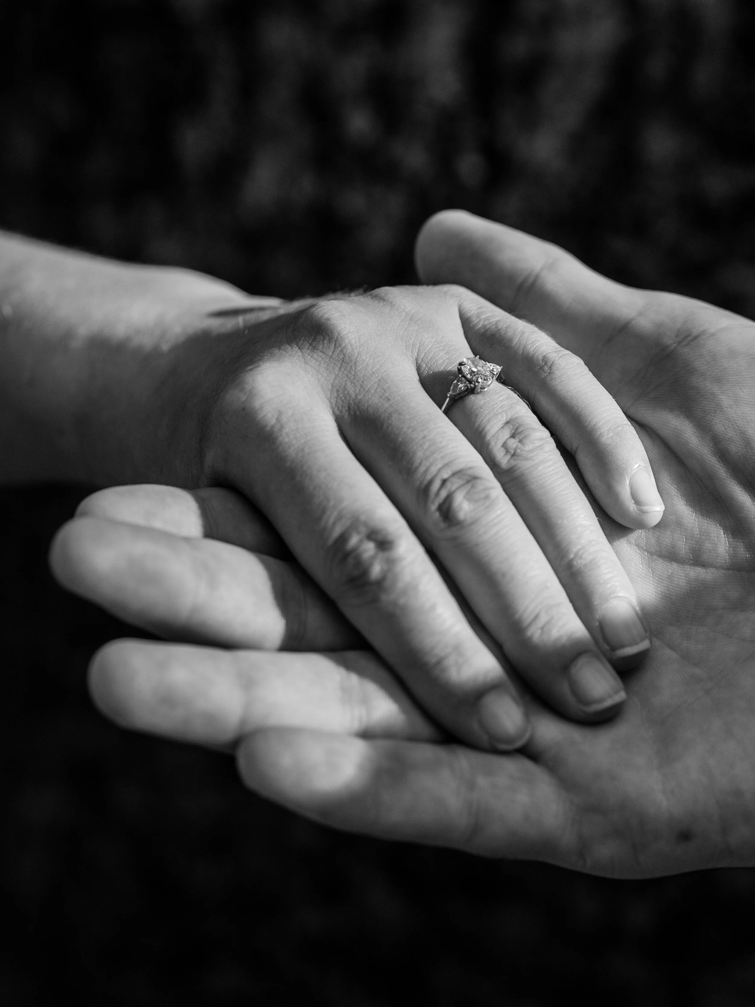 Close-up of two hands holding each other, with one hand displaying a diamond engagement ring.