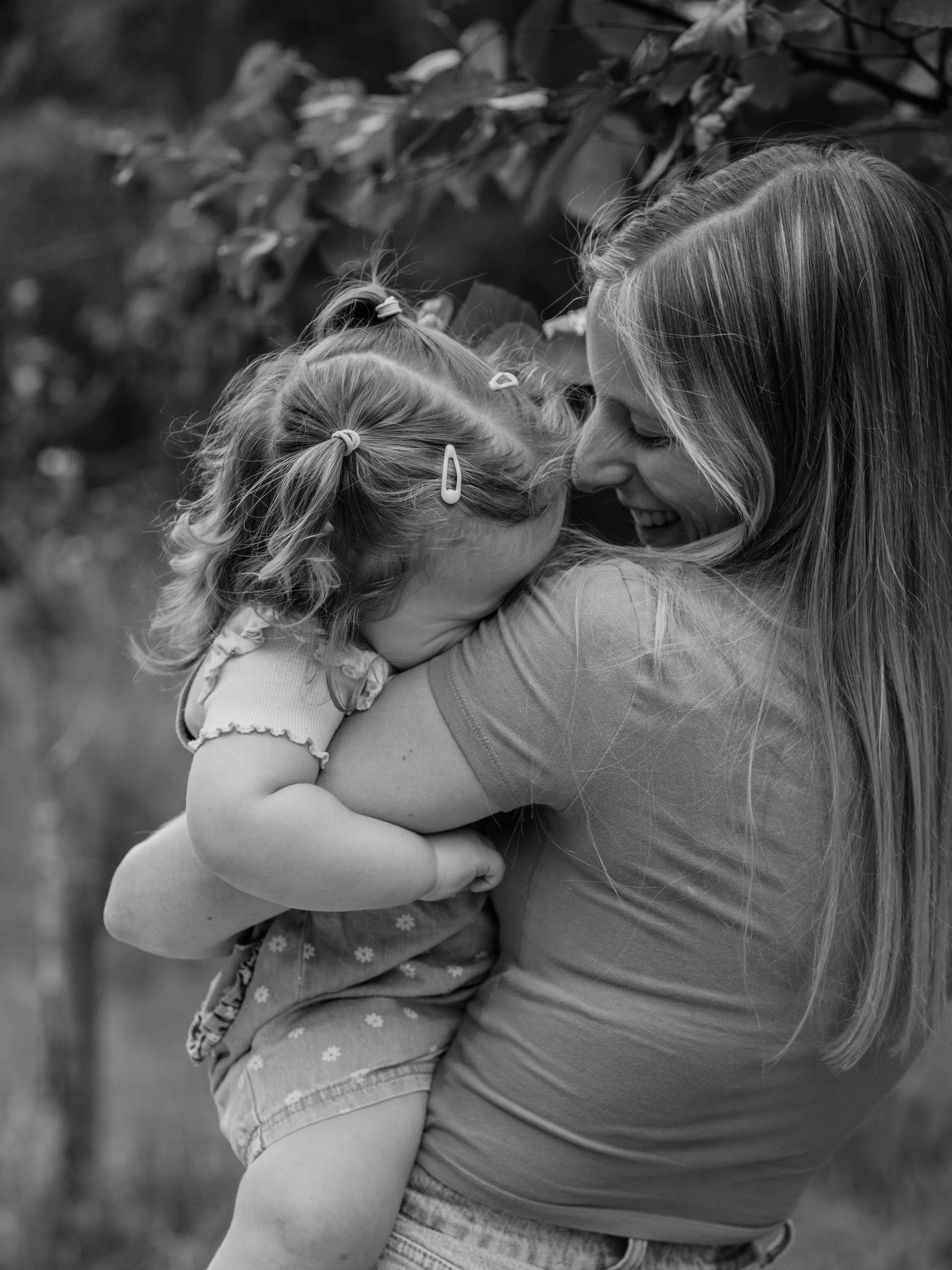 A woman and a young girl sharing a hug outdoors, smiling and embracing each other in a joyful moment.