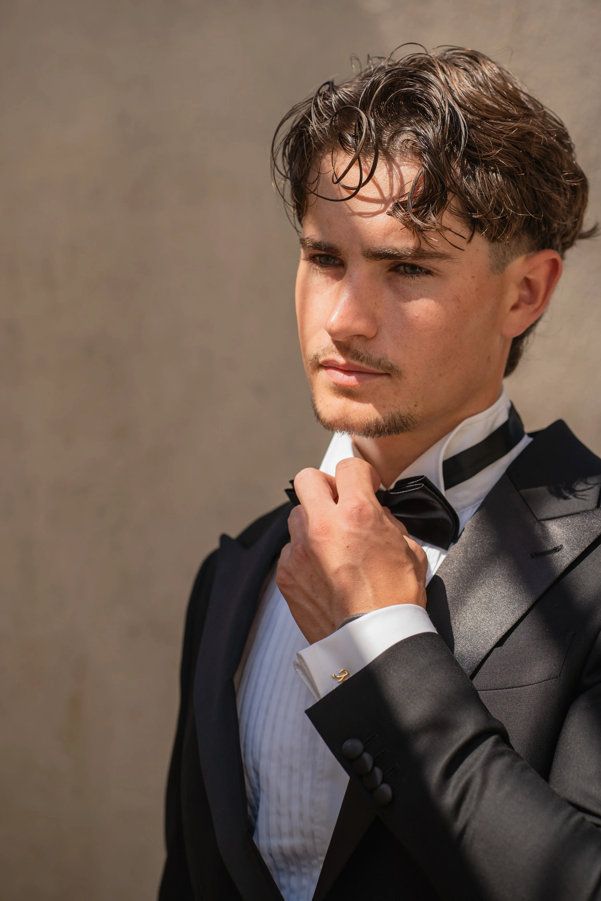 A young man adjusting a bow tie while wearing a black tuxedo with a white shirt and black bow tie.