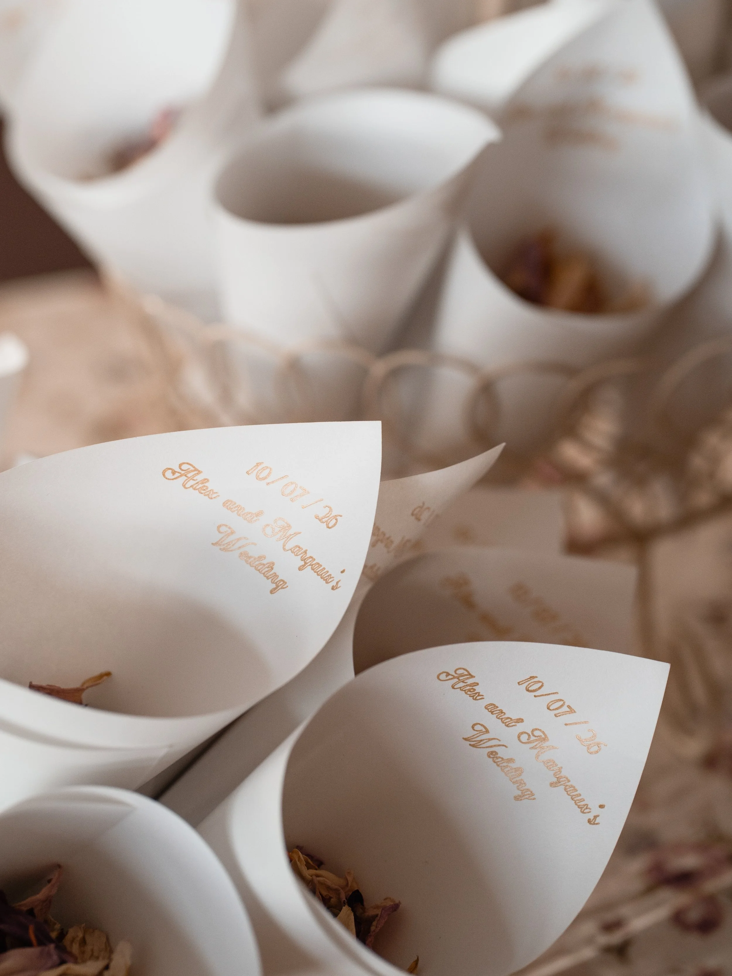 Close-up of white paper cones filled with dried rose petals, with handwritten notes visible on some of the cones.