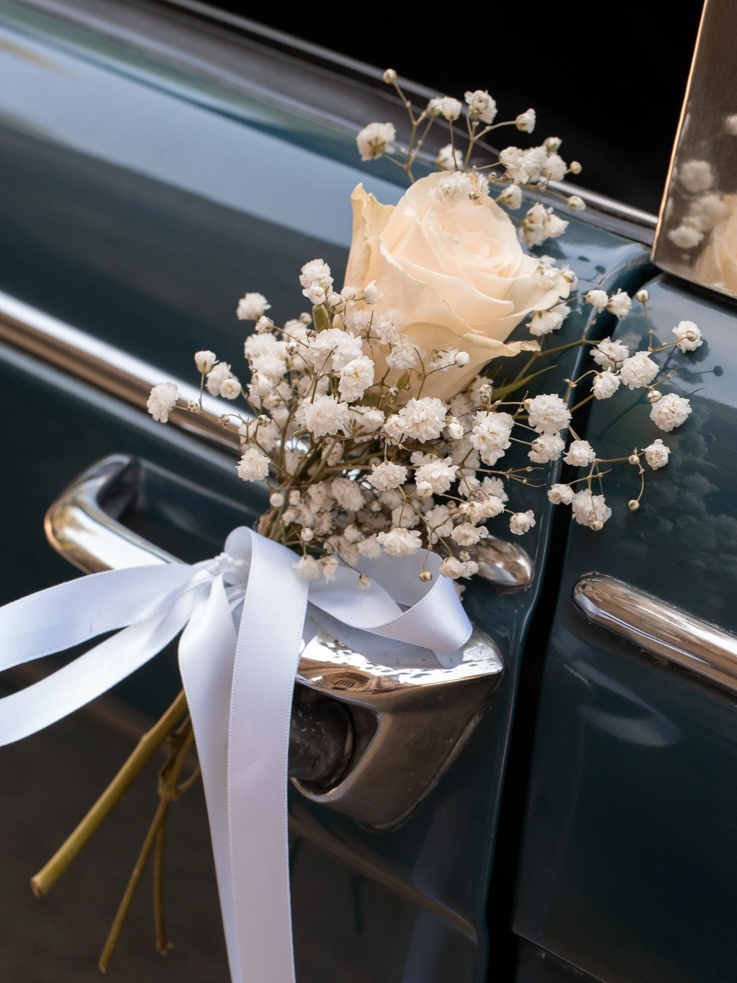 White rose and baby's breath flowers attached to a vintage car door handle with a white ribbon.