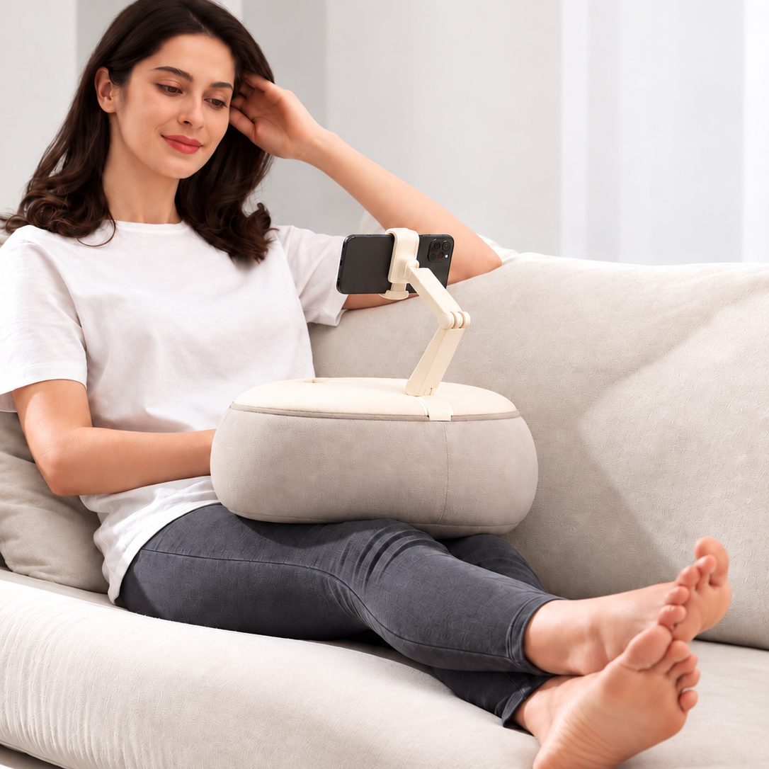 Woman relaxing on a sofa using the ALYVI V2 cushioned phone stand hands-free on her lap.