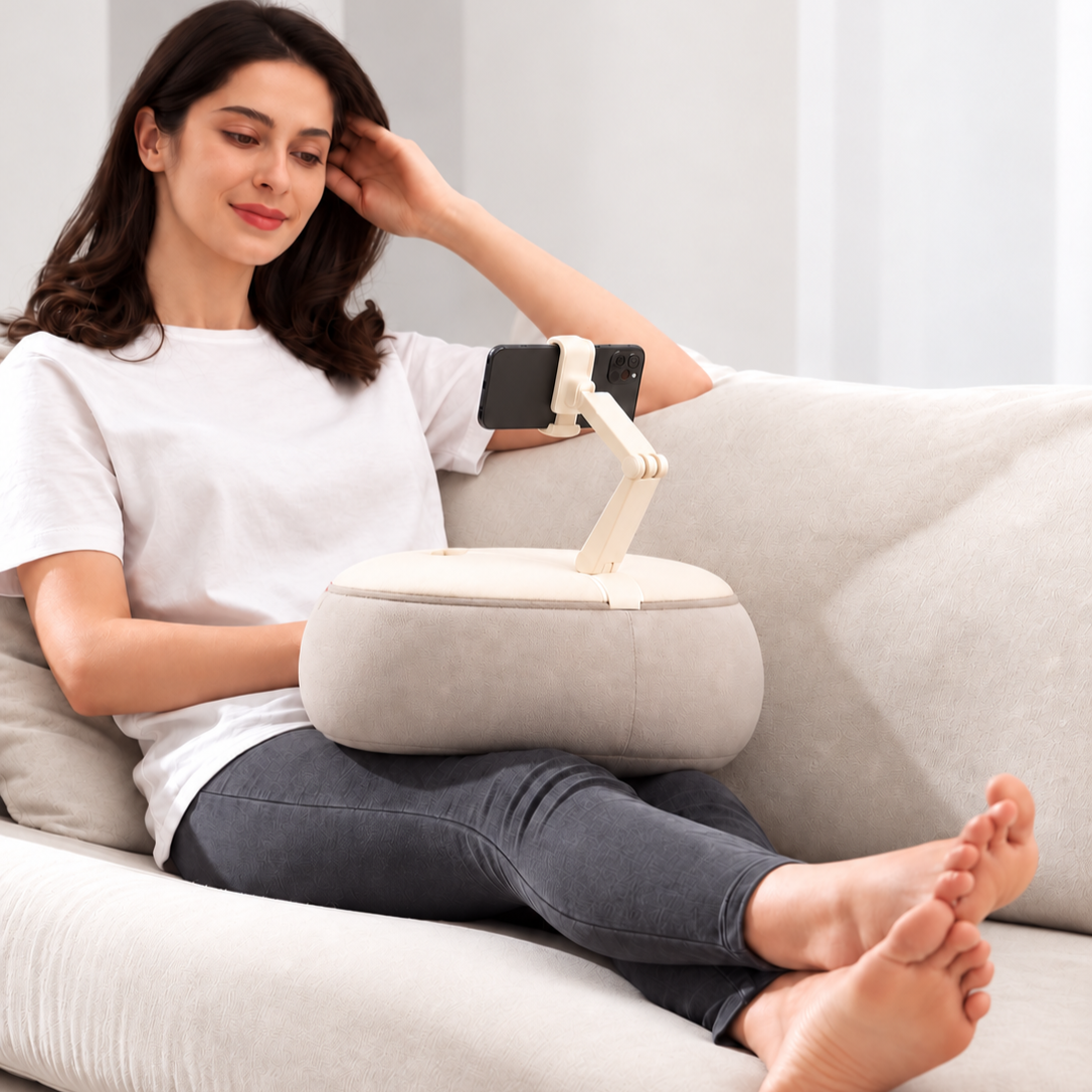 Woman relaxing on a sofa using the ALYVI V2 cushioned phone holder hands-free on her lap.