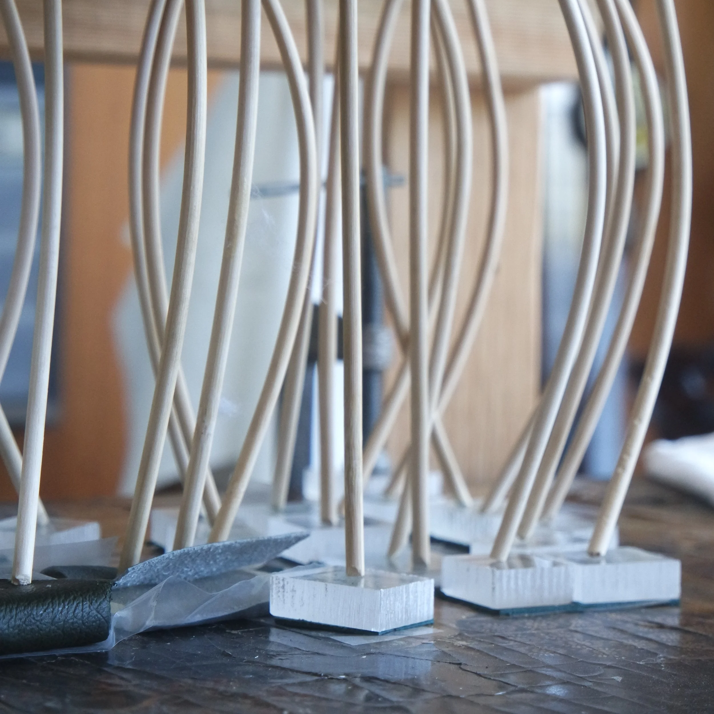 Close-up of bent bamboo sticks pressing perspex blocks against an uneven lacquered surface.