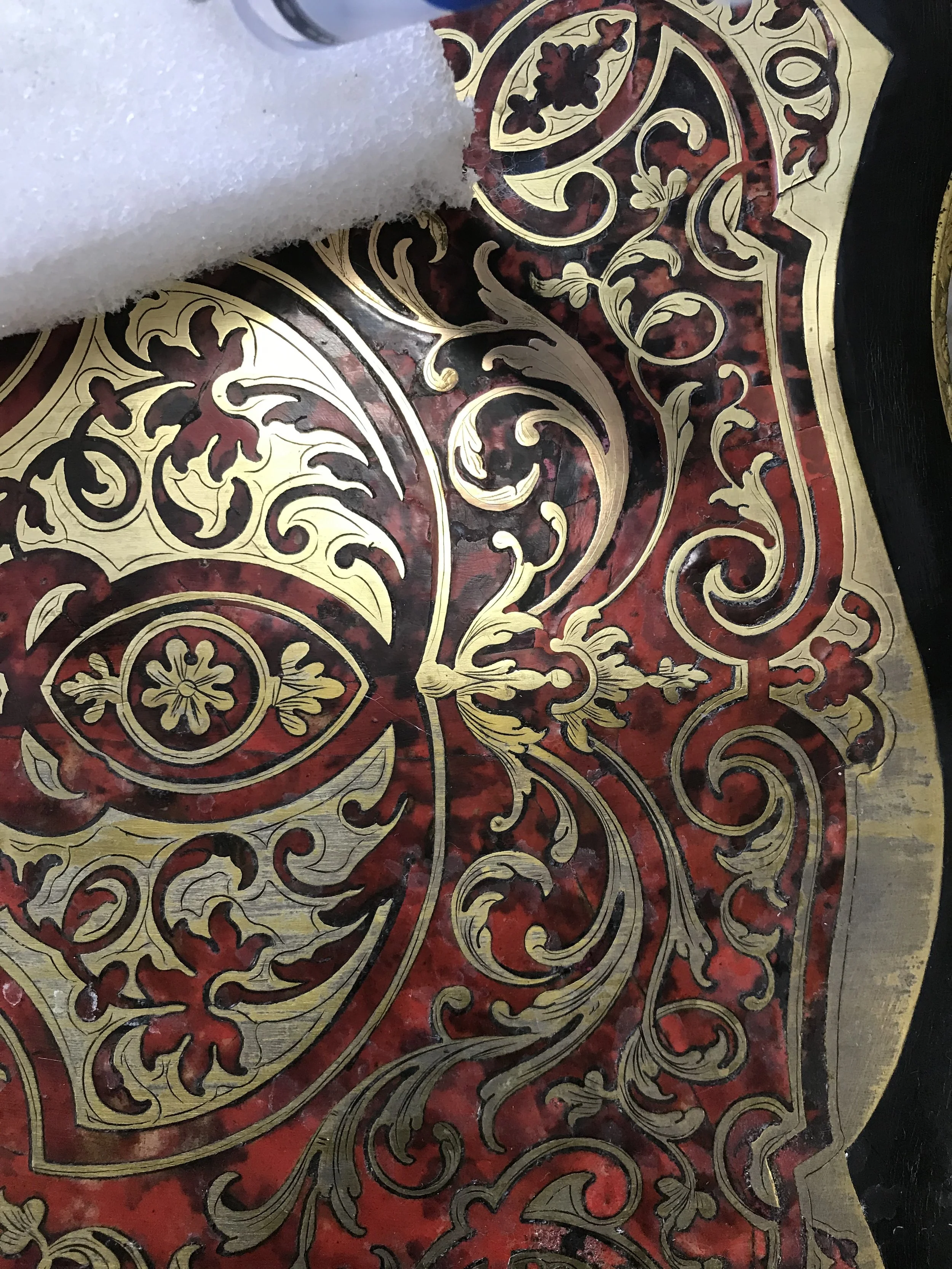 A decorative ornate black and gold pattern on a red background with intricate floral and scroll designs.