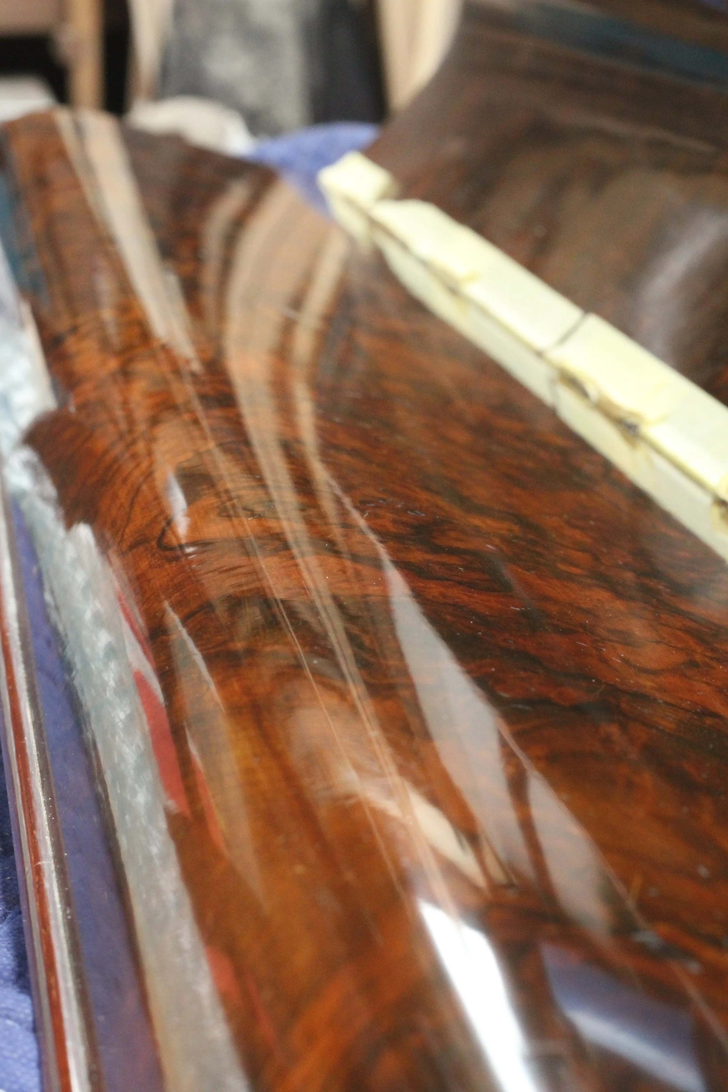 Close-up of a polished curved rosewood piano componant with blurred background.