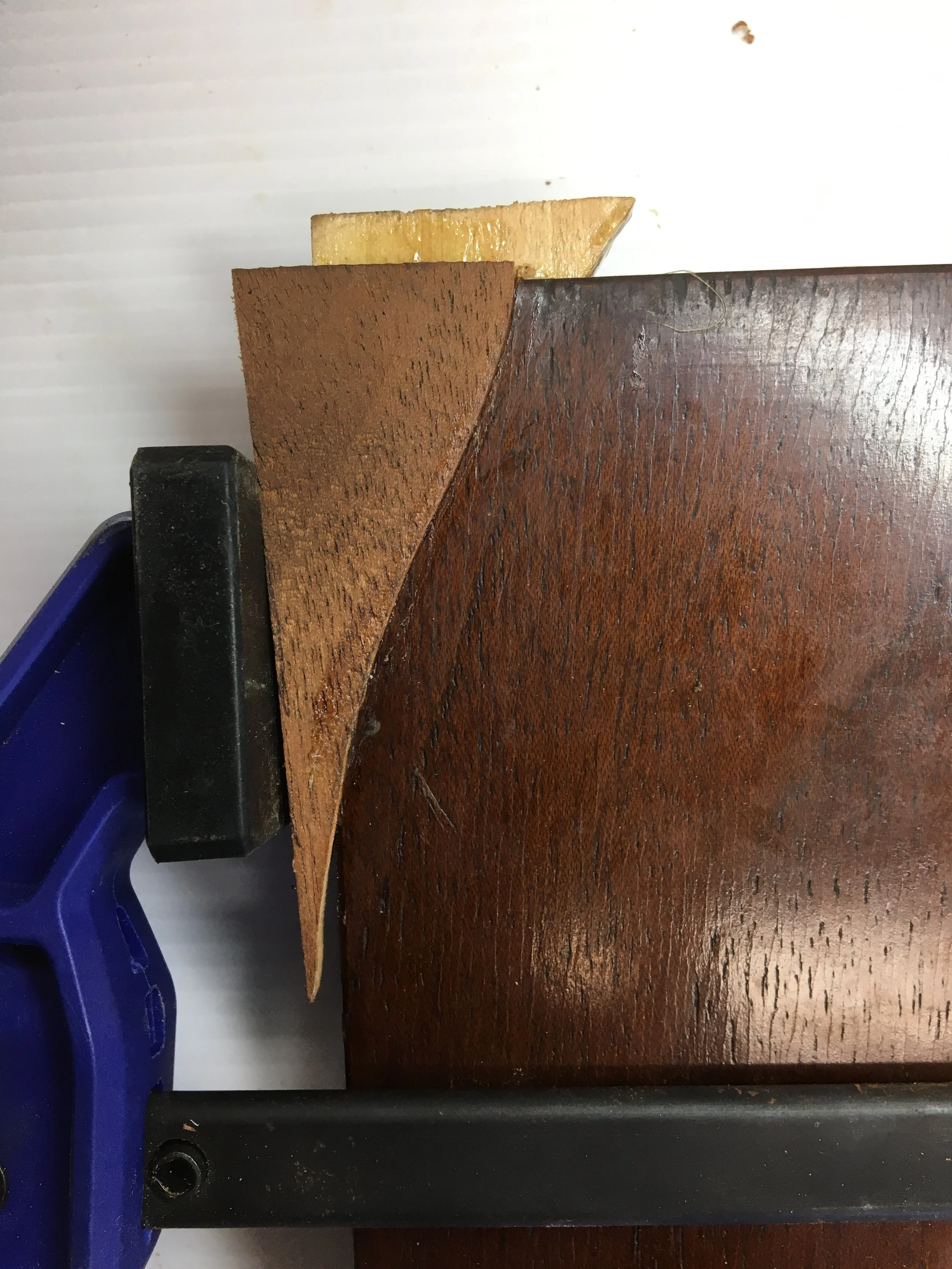 A close-up image of a wooden panel with a carefully cut timber patch being glued and clamped to it.