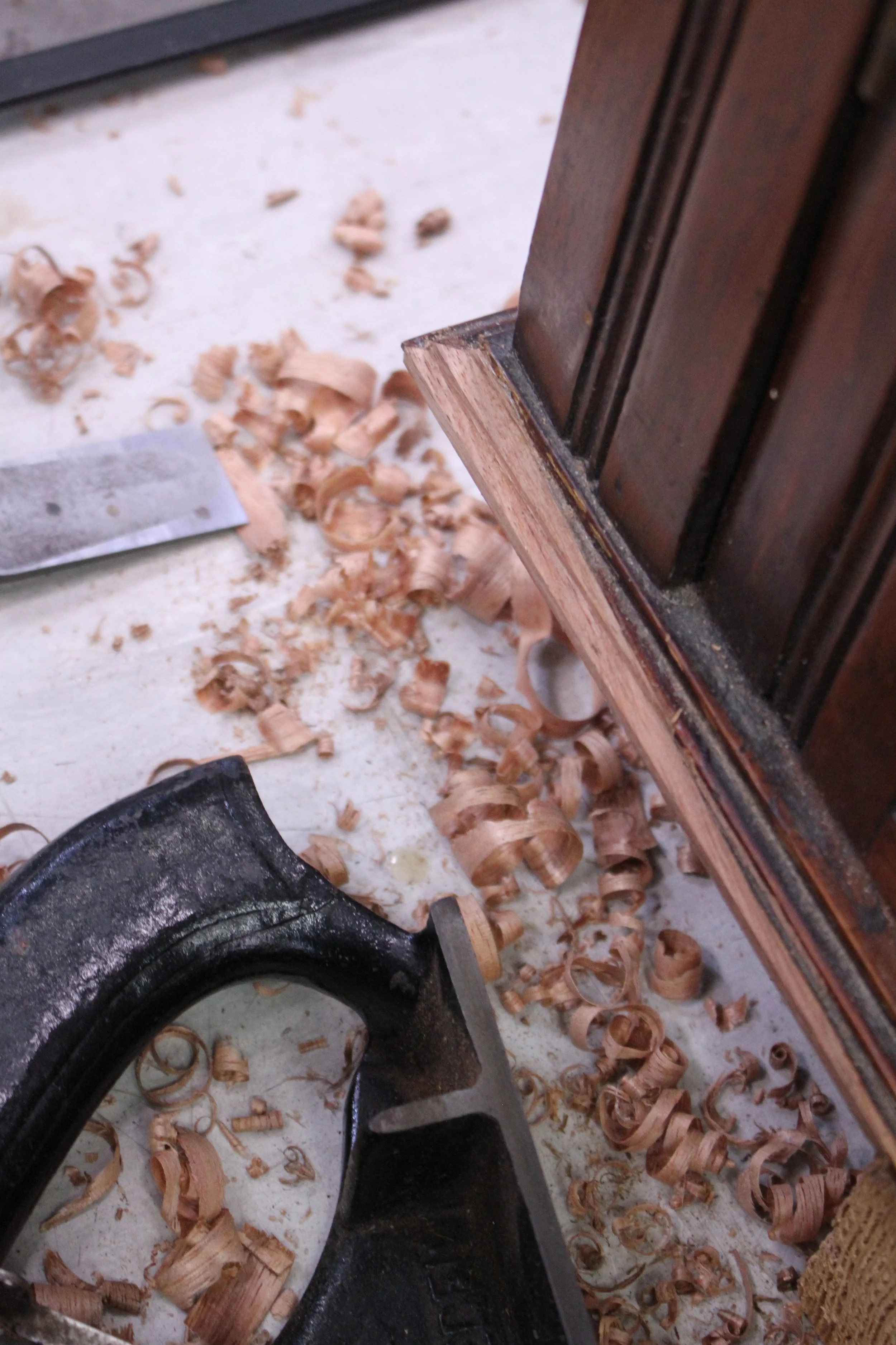 Close-up of woodworking tools, wood shavings, and a piece of wood in a woodworking shop.
