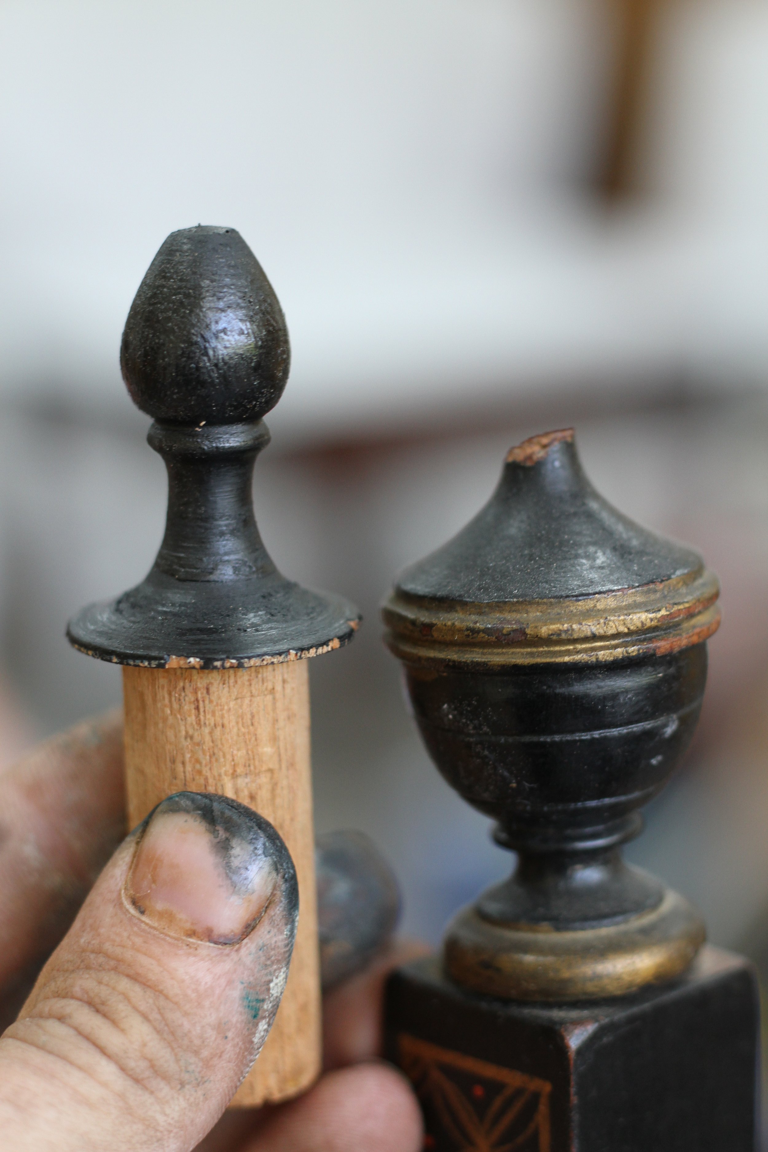 A person holding the turned top of a wooden wooden finial next to a broken finial.