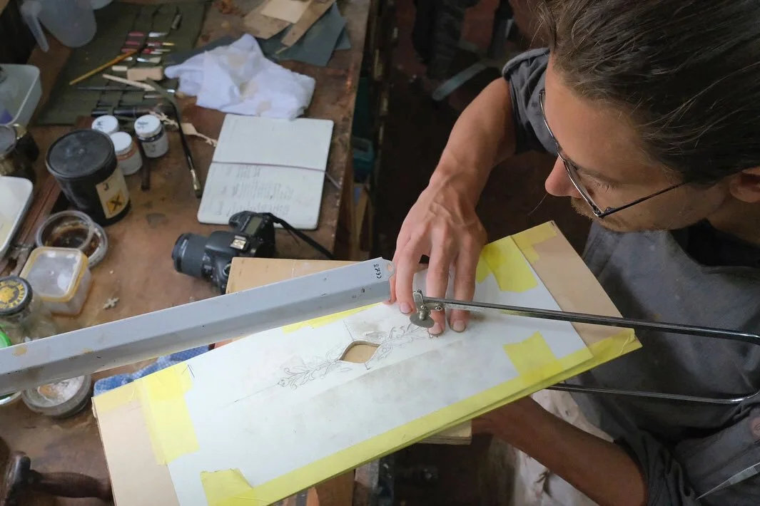 A person working on a woodworking project, using a coping saw to cut a marquetry pattern.