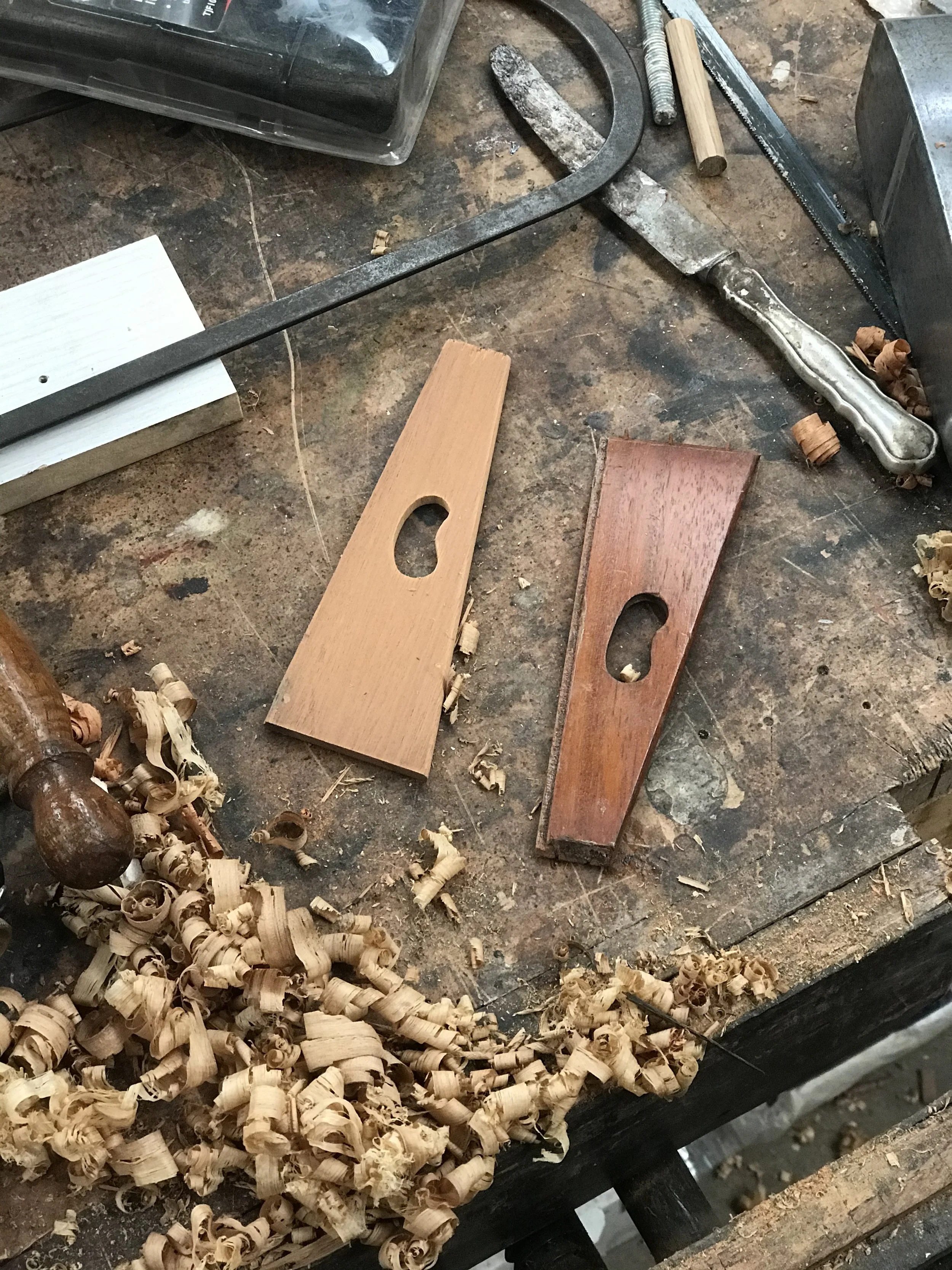 A woodworking workbench with wood shavings, two hand saws, and various tools and wood pieces.