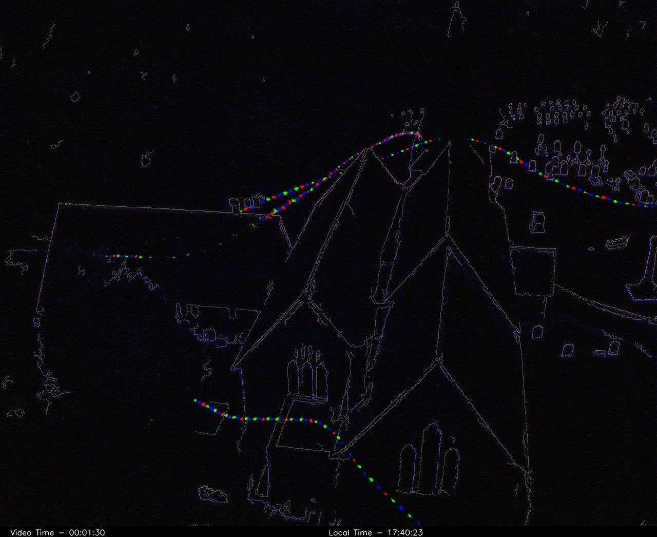 Outline of a church and surrounding buildings, with a string of colorful lights displayed in a light display presentation at night.