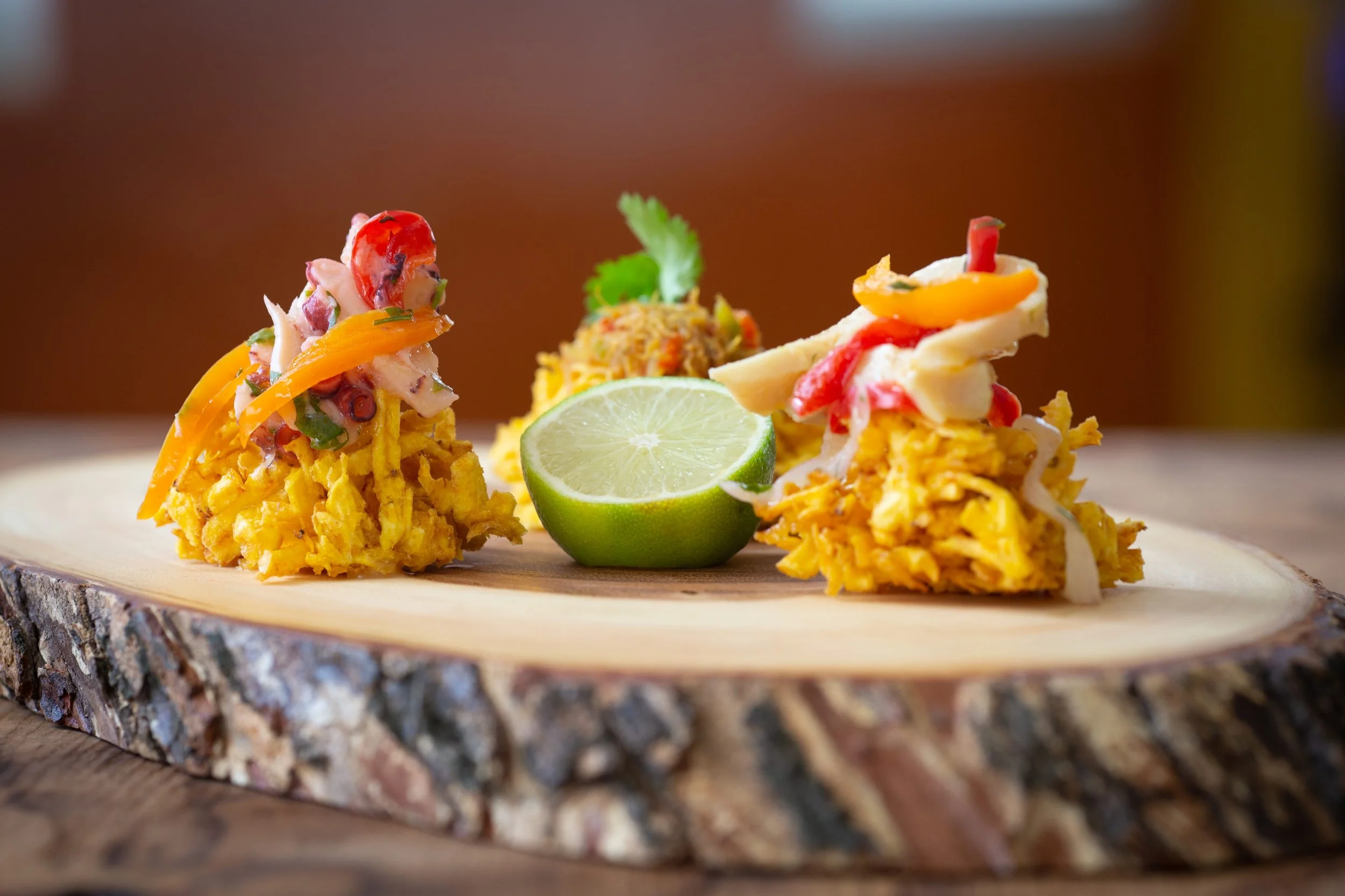 Corn-based Mexican dish topped with vegetables, cheese, a slice of lime, and garnished with cilantro, served on a wooden surface.