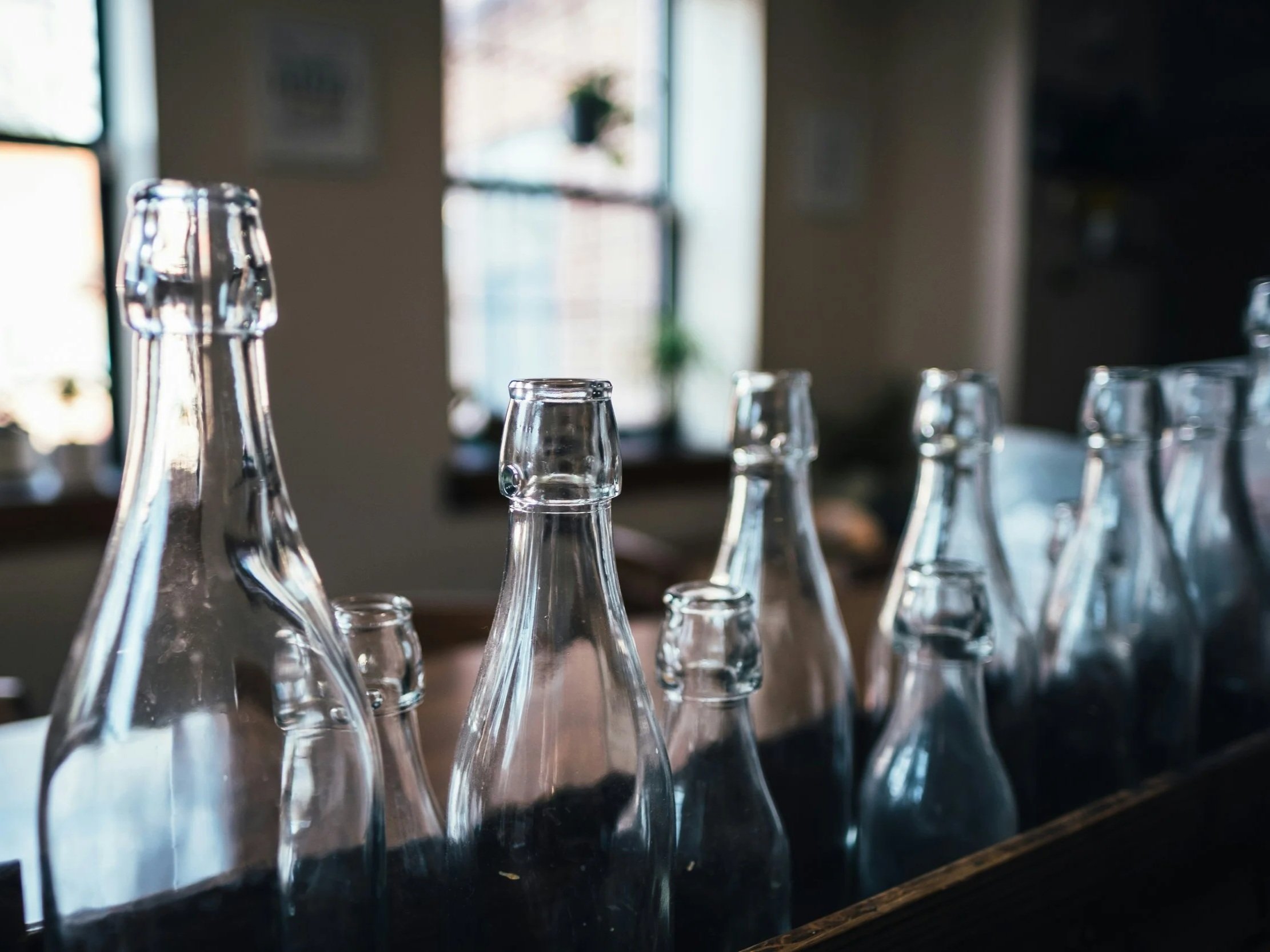 Botellas reutilizables de cristal en una mesa junto a una ventana que permite la entrada de luz natural en lo que parece ser un restaurante o cafetería.