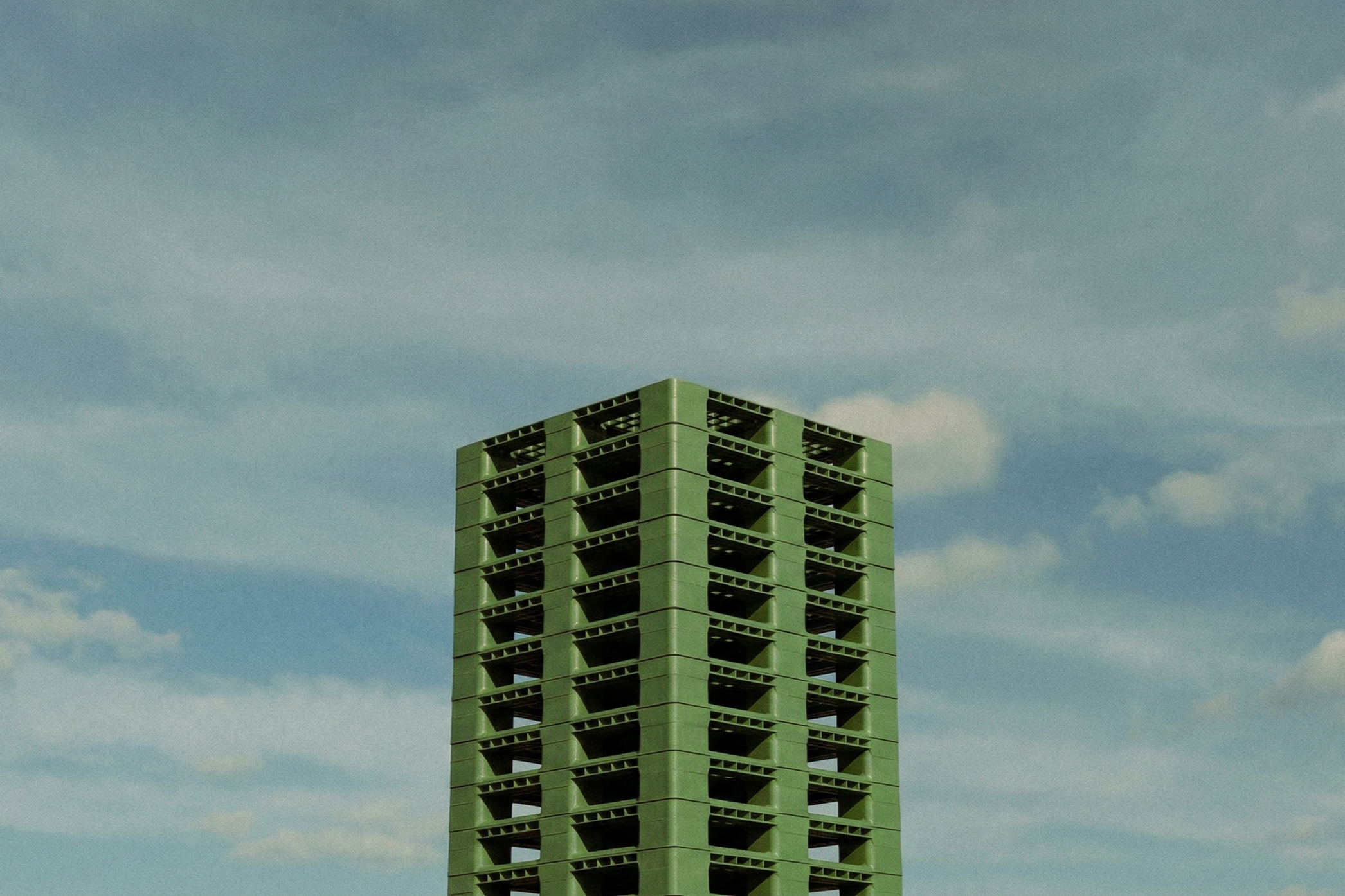 Bloque de palets reutilizables de plástico verde bajo un cielo despejado con algunas nubes.