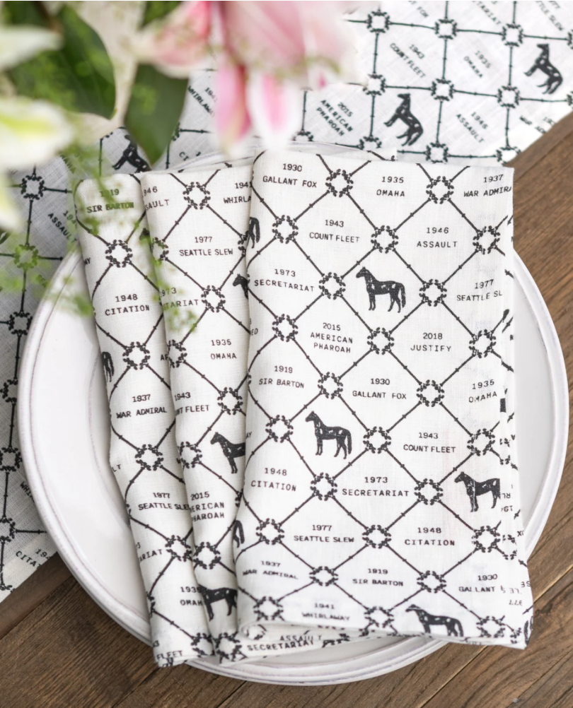 A floral napkin with black timeline text and images of dogs, placed on a white plate with greenery nearby.