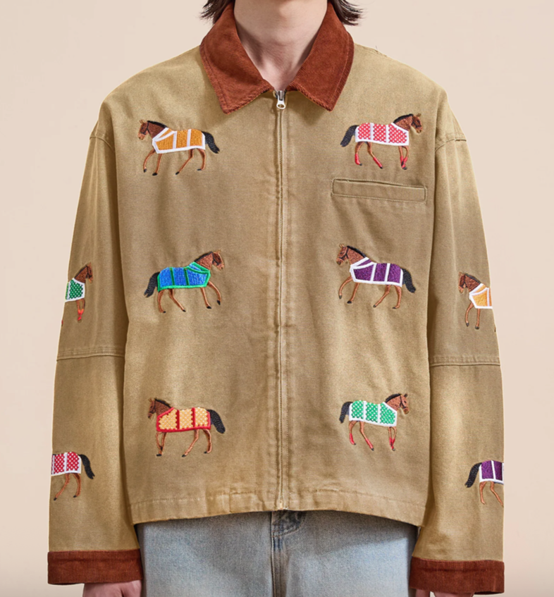 Beige jacket with embroidered horses in colorful saddle blankets, brown collar, and light blue jeans.