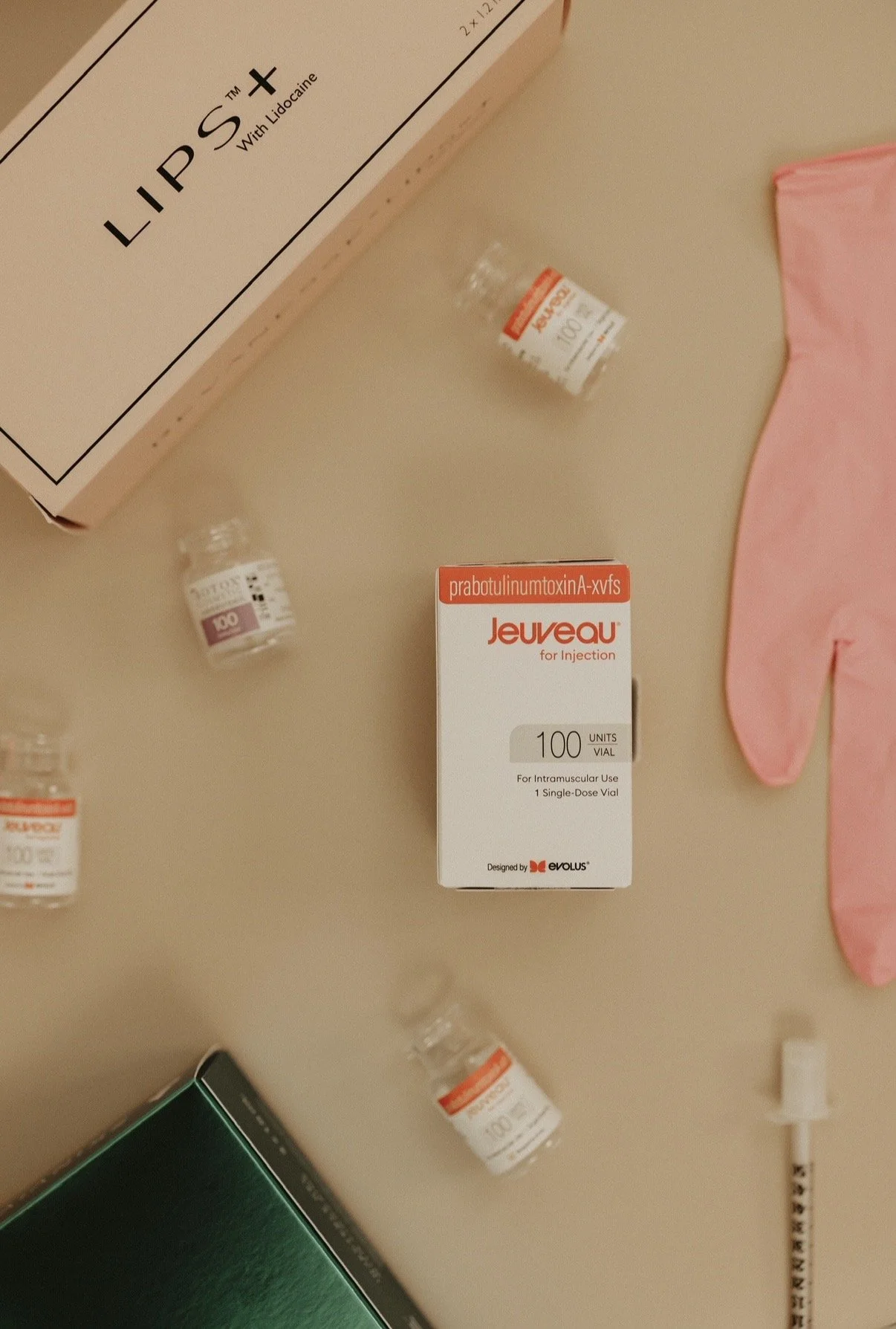 A box labeled Jeuveau for injection with 100 units vial, along with several small vials of medication and pink medical gloves on a beige surface.