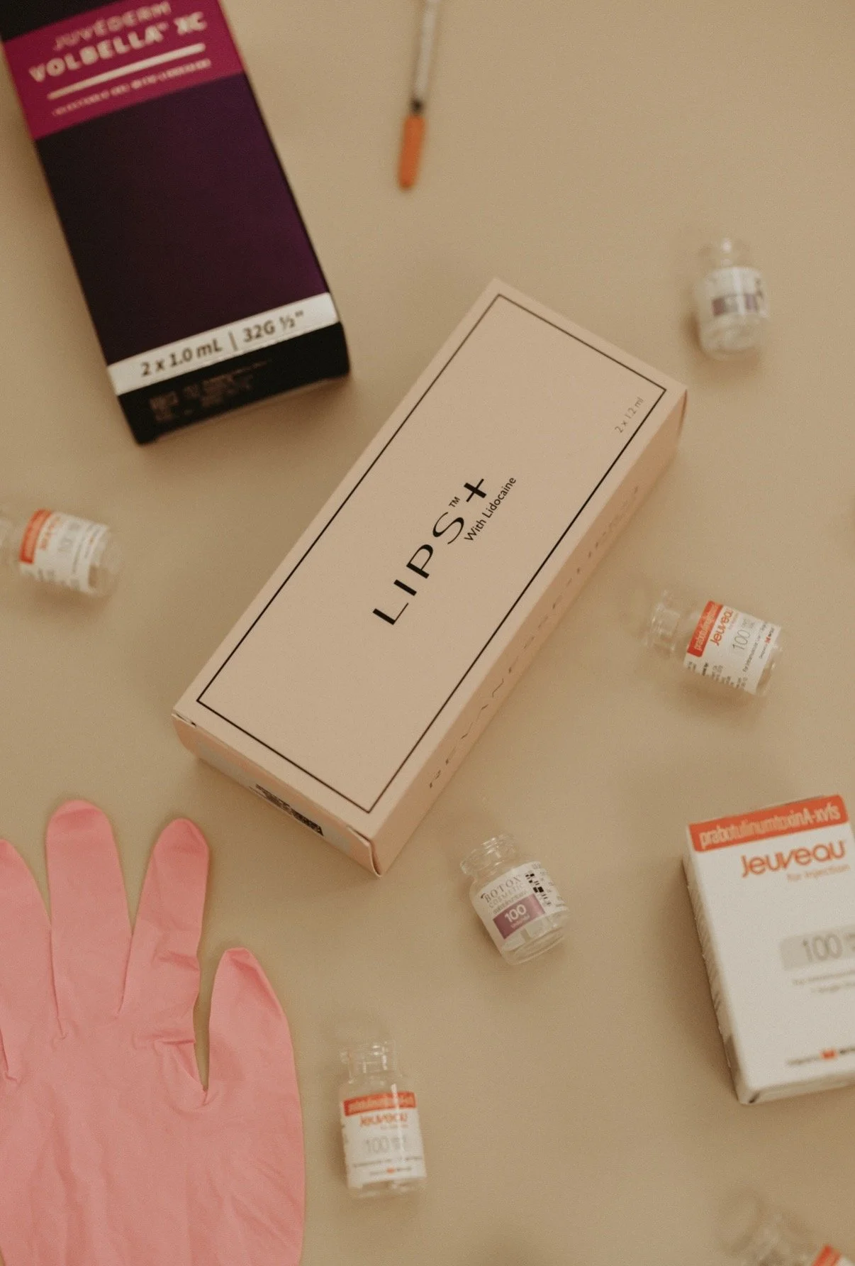 Medical supplies on a beige surface, including boxes labeled "LIPS+" with lidocaine, small vials, and a pink latex glove.