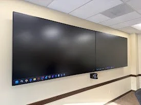 Two large flat screen monitors mounted on a beige wall in a conference room.