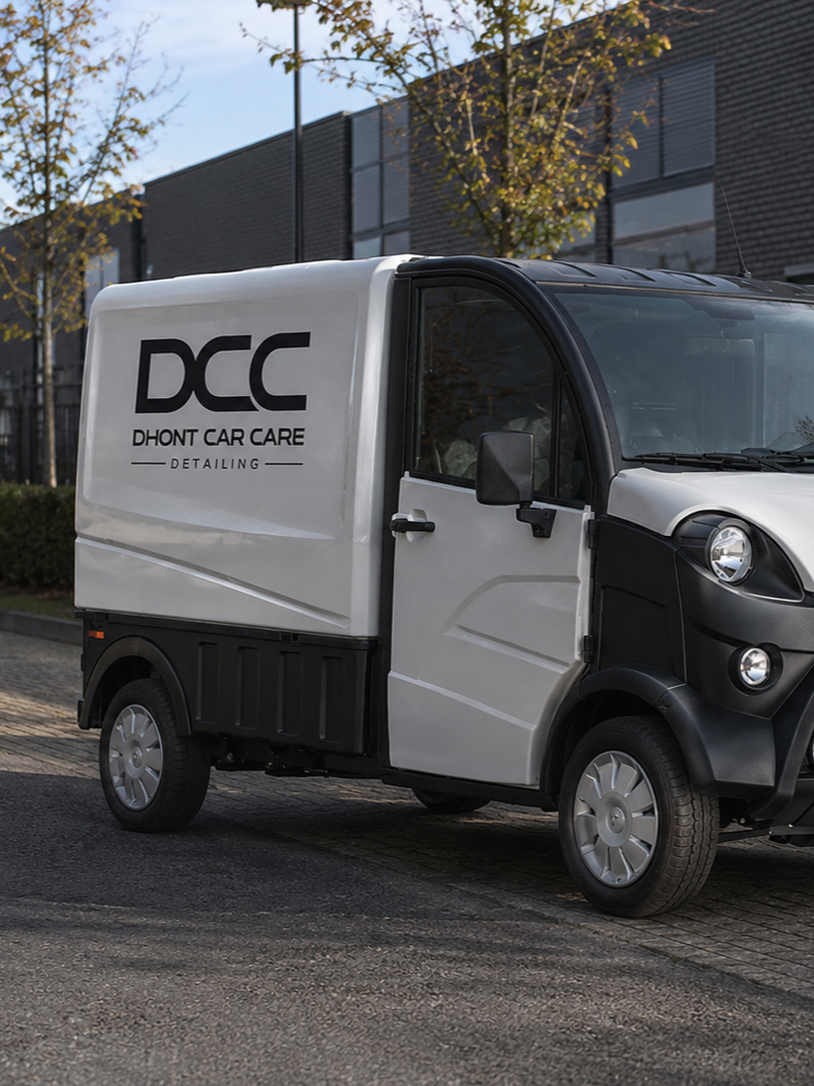 Small delivery vehicle with DCC Dhont Car Care Detailing logo parked on a street with trees and modern building in the background.