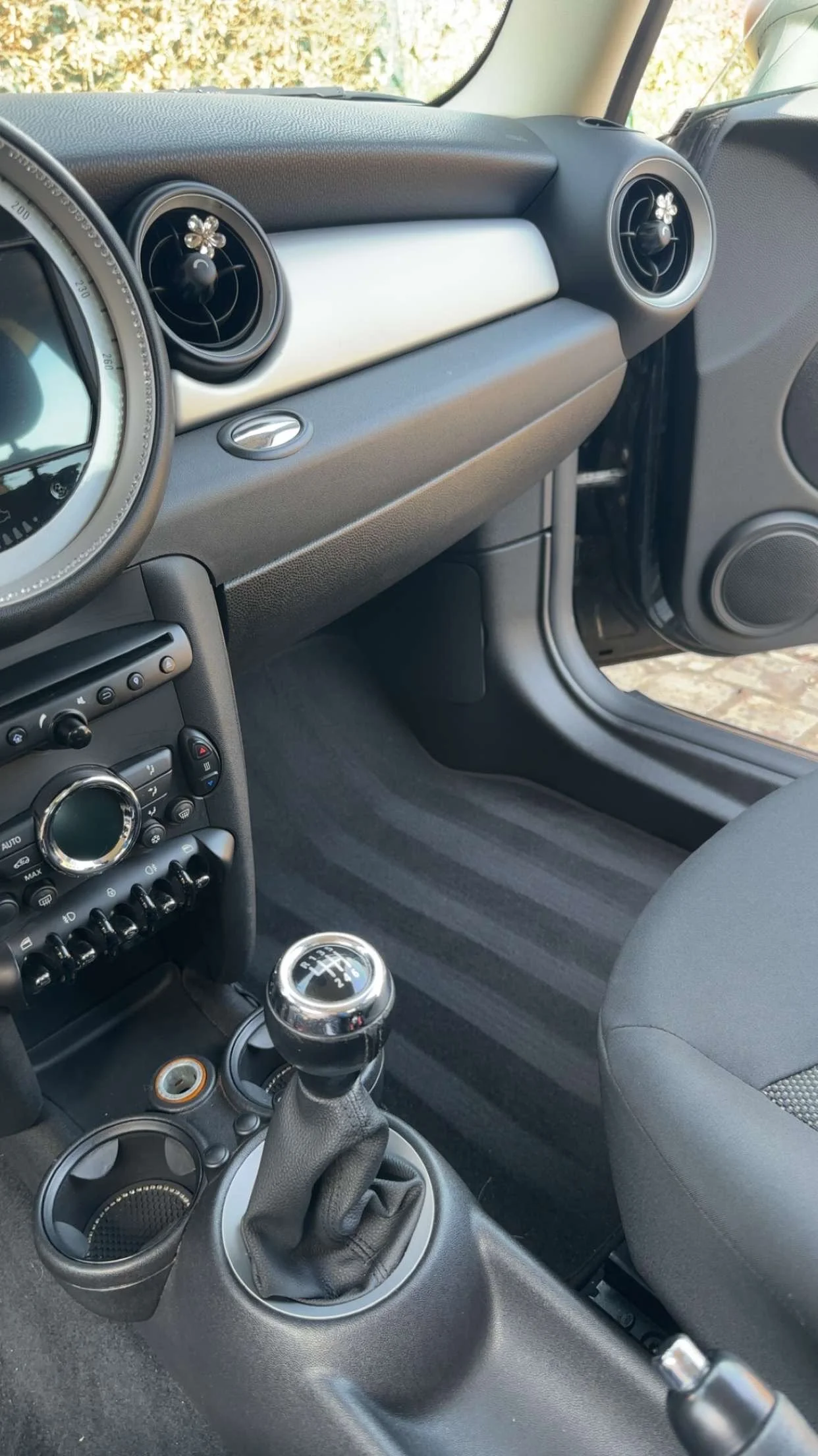 Interior of a car showing the dashboard with air vents decorated with small flower-shaped ornaments, gear shift, and part of the center console.