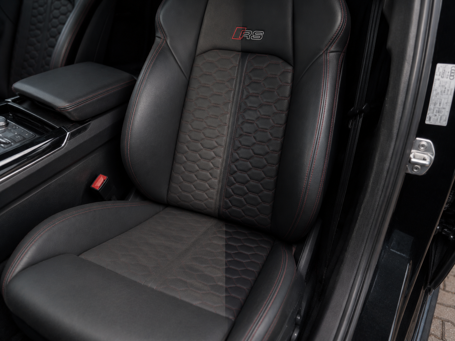 Close-up of a black car seat with red stitching and honeycomb pattern, inside a luxury vehicle.