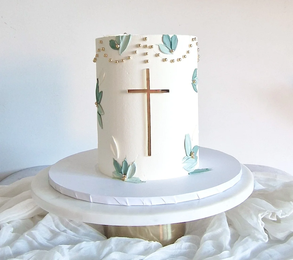 Elegant christening cake with textured buttercream, gold cross and sage green leaf detailing