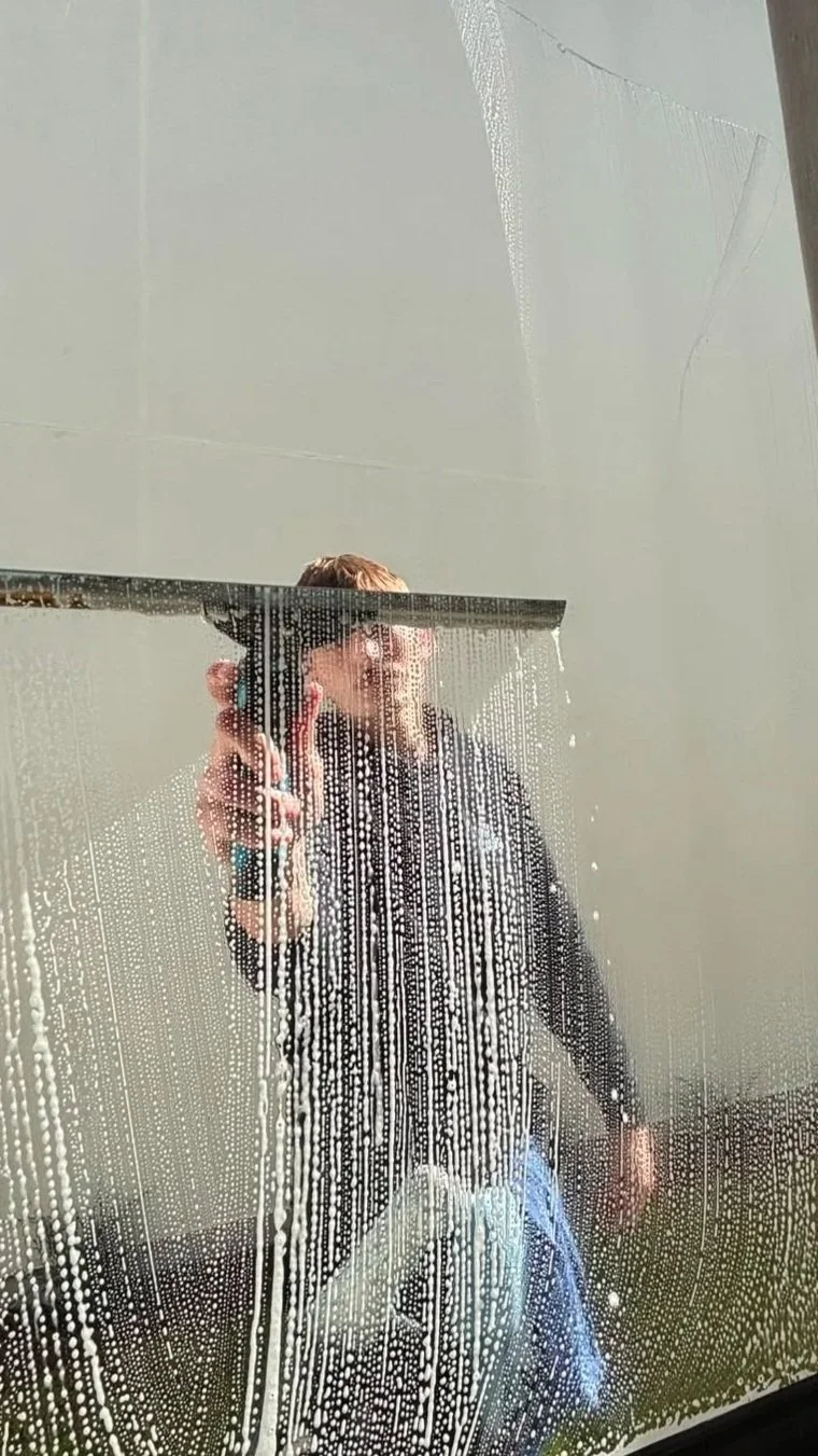 Person cleaning a mirror with soap and a squeegee.