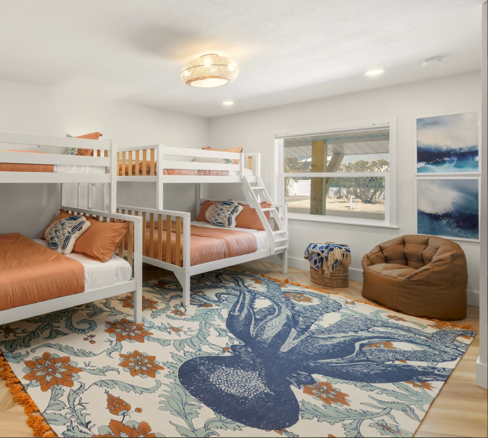 Bedroom with white bunk beds with orange bedding, a patterned area rug, and a window showing a beach scene outside.