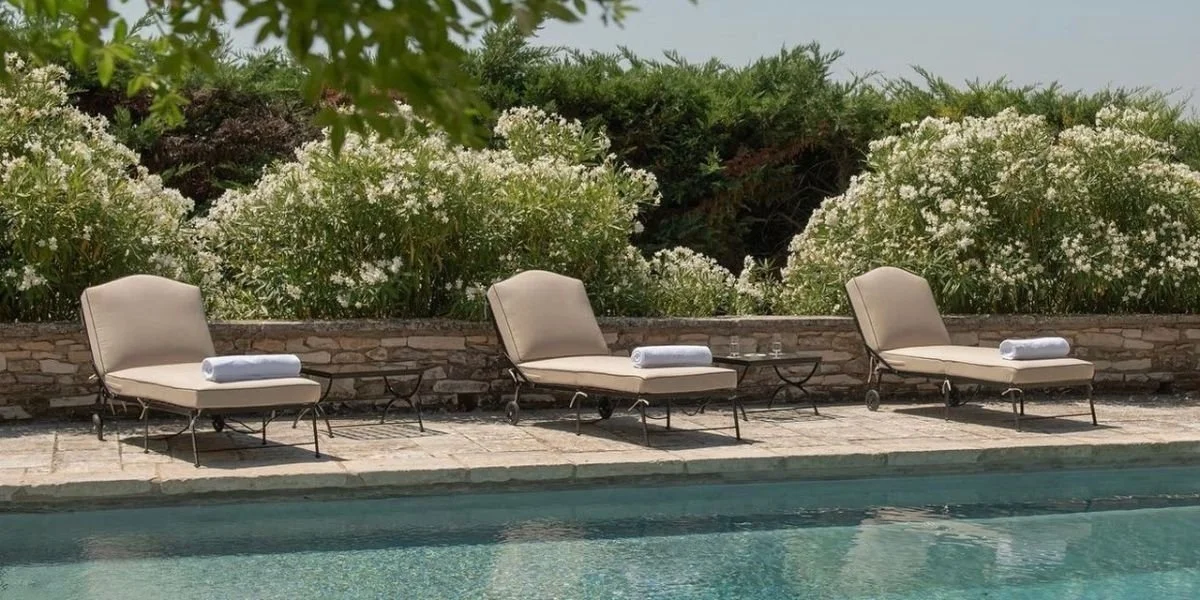 Poolside lounge chairs with rolled towels and small tables against a backdrop of blooming bushes and trees.