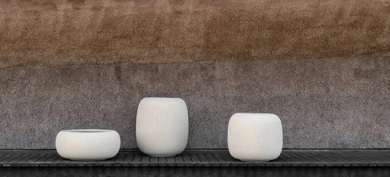 Three white modern outdoor planters of different sizes placed on a wooden platform against a textured wall.