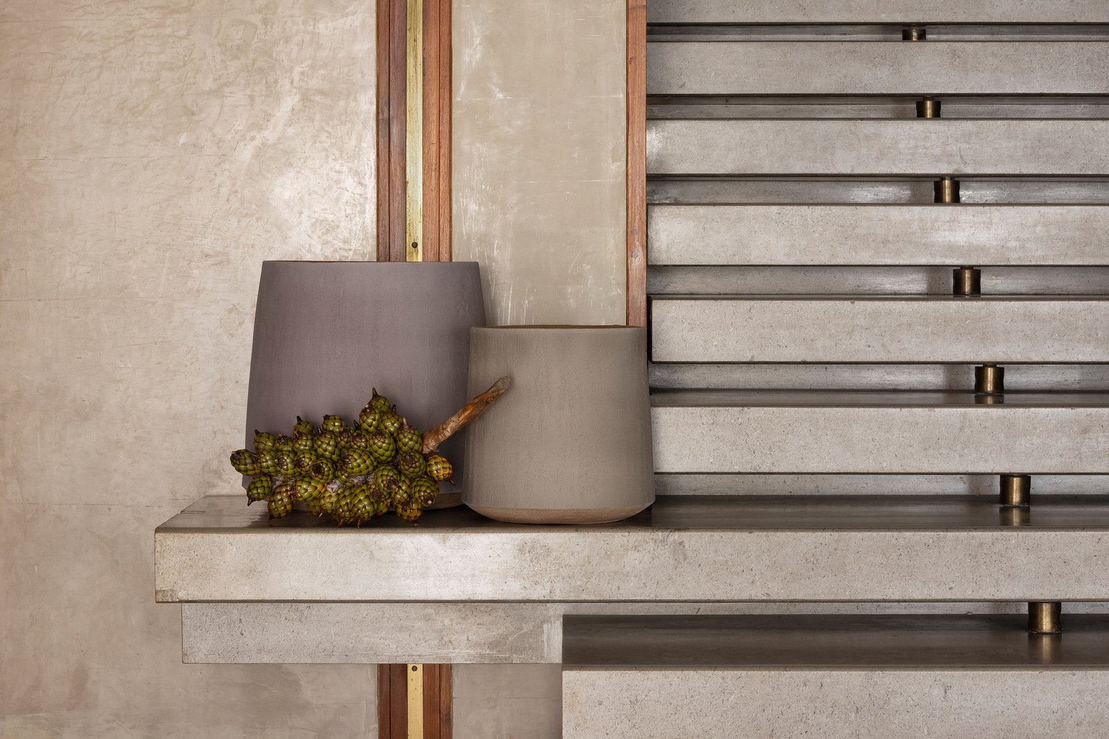 A still life interior scene featuring two gray lamps and a bunch of green decorative artichokes on a concrete surface, with a textured beige wall and wooden trim in the background.